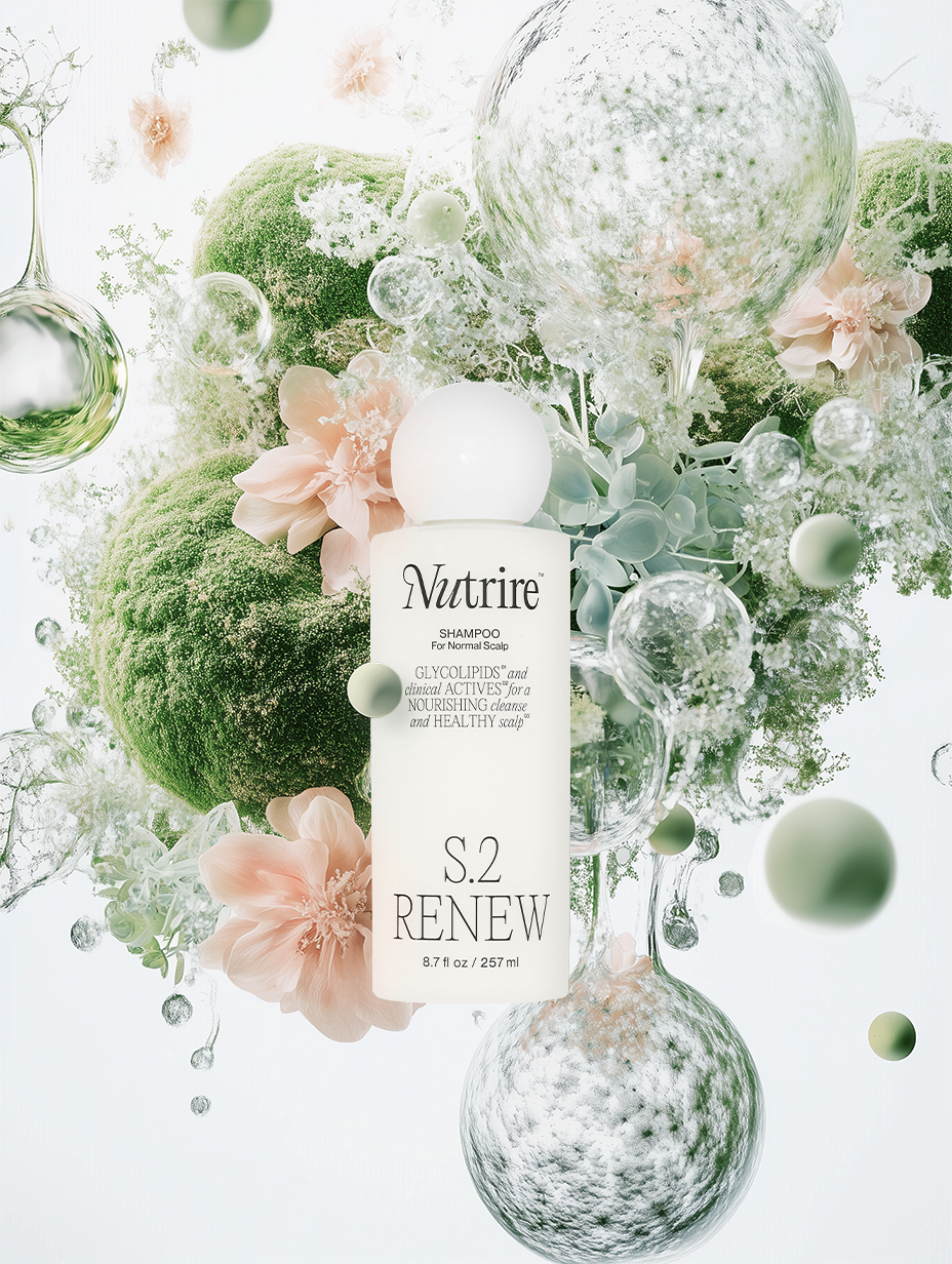 A white shampoo bottle labeled 'Nutrire S.2 Renew' surrounded by green moss, pink flowers, and floating glass bubbles on a light background.