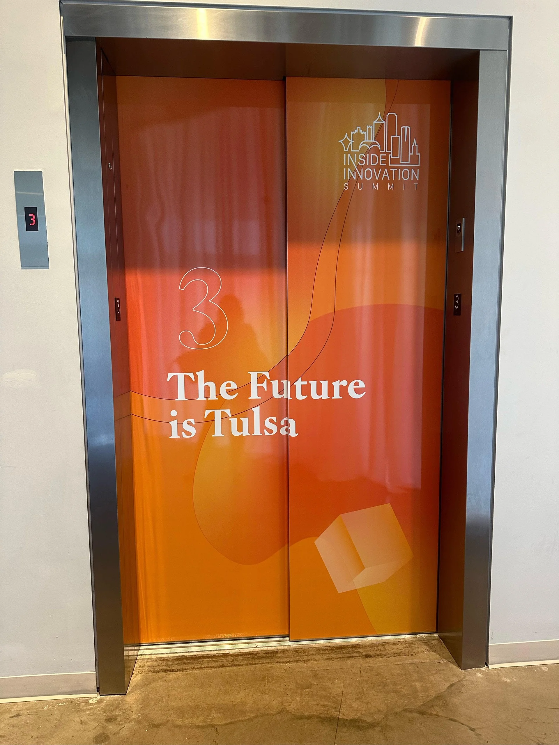 Elevator with orange doors branded with the Inside Innovation Summit logo and the text "3 The Future is Tulsa".