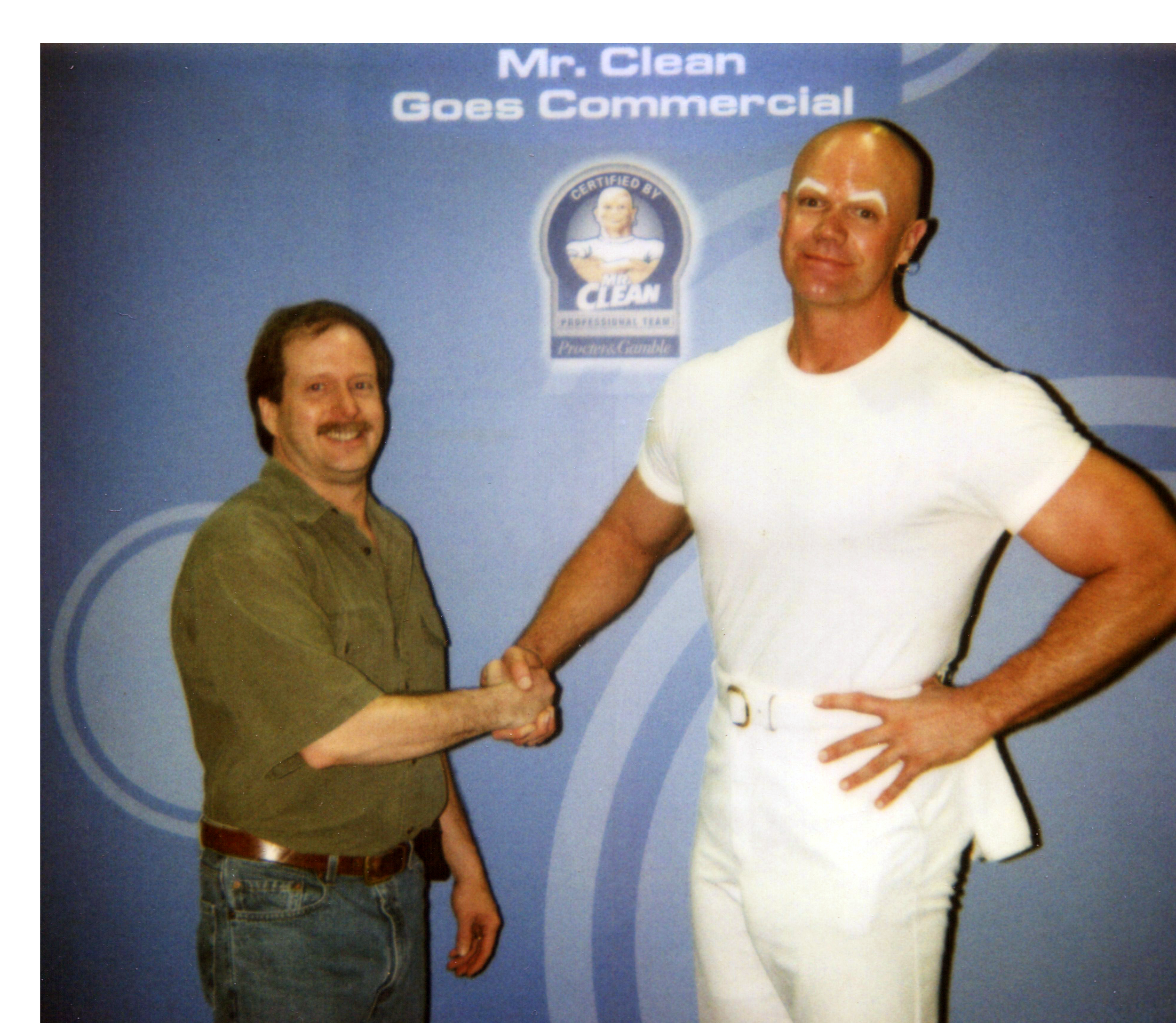 Dan and Mr. Clean shaking hands in front of a blue backdrop that says "Mr. Clean Goes Commercial."