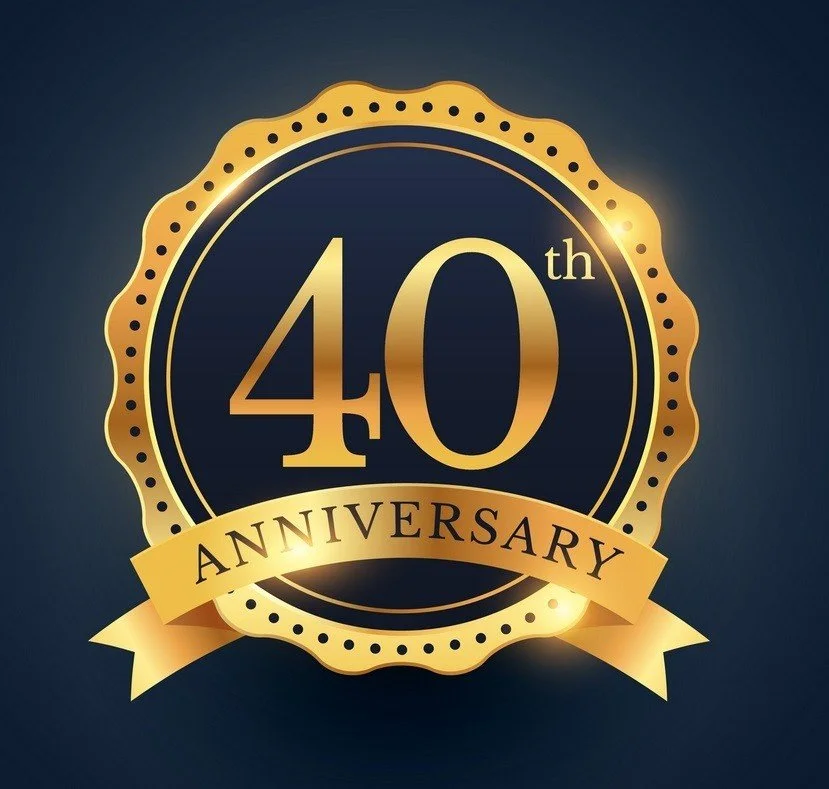 Gold and black 40th anniversary badge with a ribbon reading 'Anniversary' on a dark background.