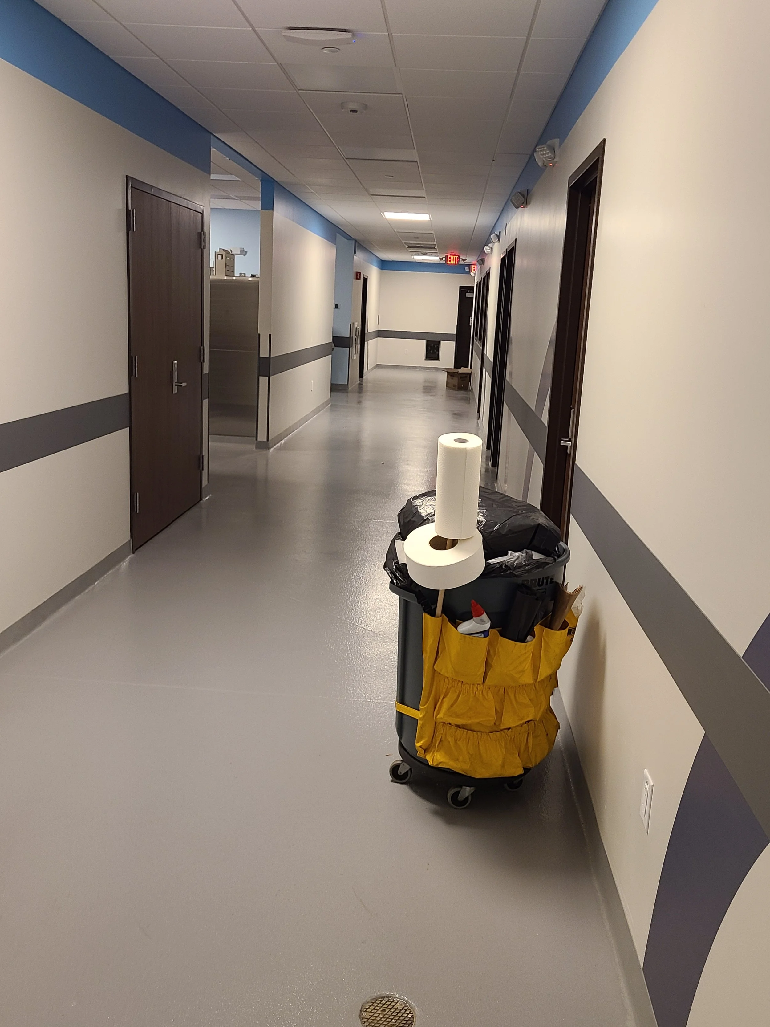 Empty hospital hallway with a cleaning cart containing paper towels and cleaning supplies.