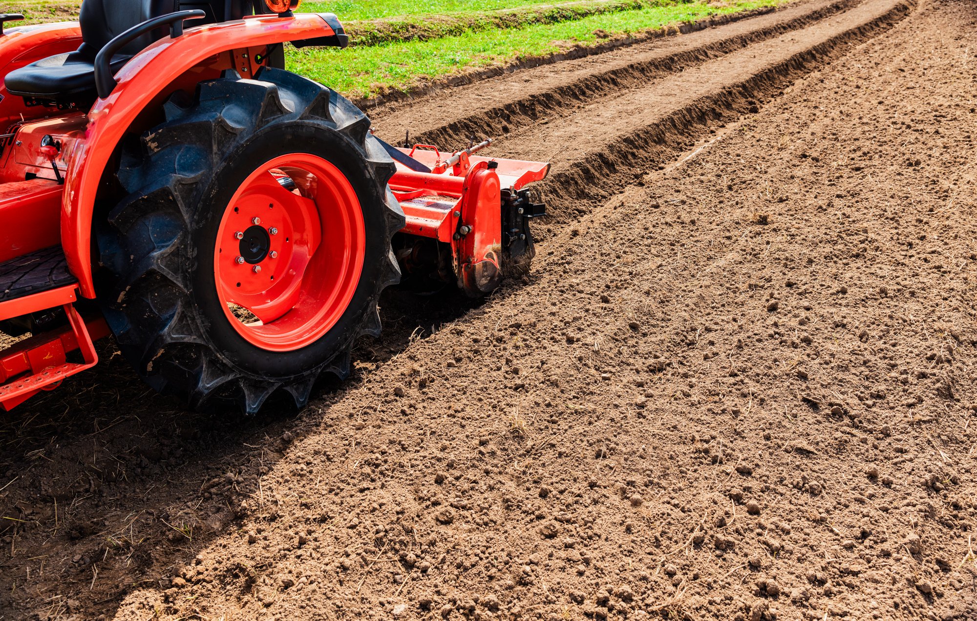 A red tractor tilling and preparing the soil in a farm field.