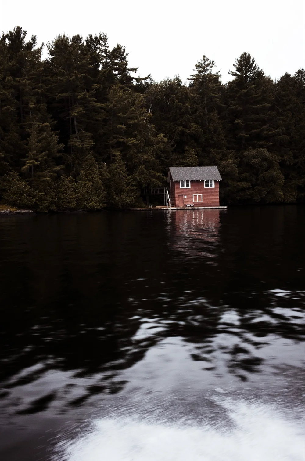Gingerbread Boathouse by MrSpacetime: a red boathouse beneath dark pines on Lake Joseph