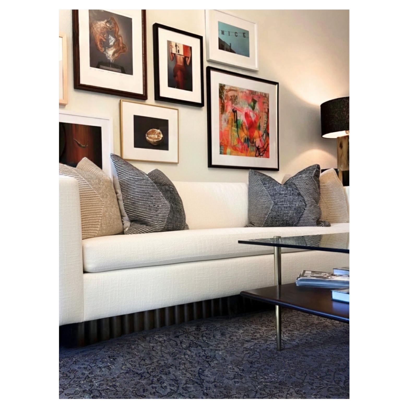A modern living room designed by Austin interior designer HOLLEYHOUSE with a white sofa and six throw pillows in various shades of gray and beige. The wall behind the sofa features a gallery of framed art and photographs.