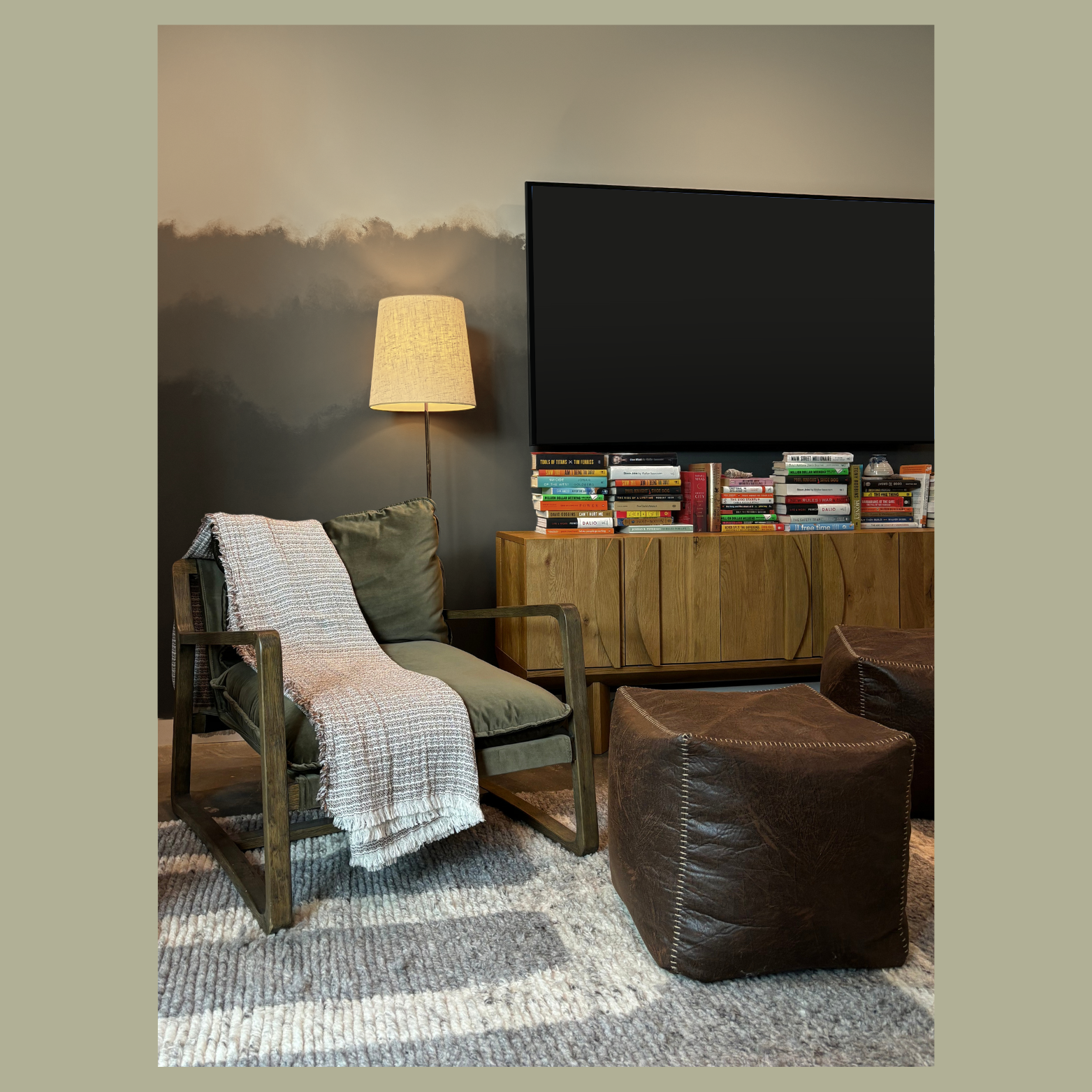 Living room designed by Austin interior designer HOLLEYHOUSE with a wooden armchair with green cushions and a beige throw blanket, a tall floor lamp with a beige lampshade, a wooden cabinet with a large stack of books.
