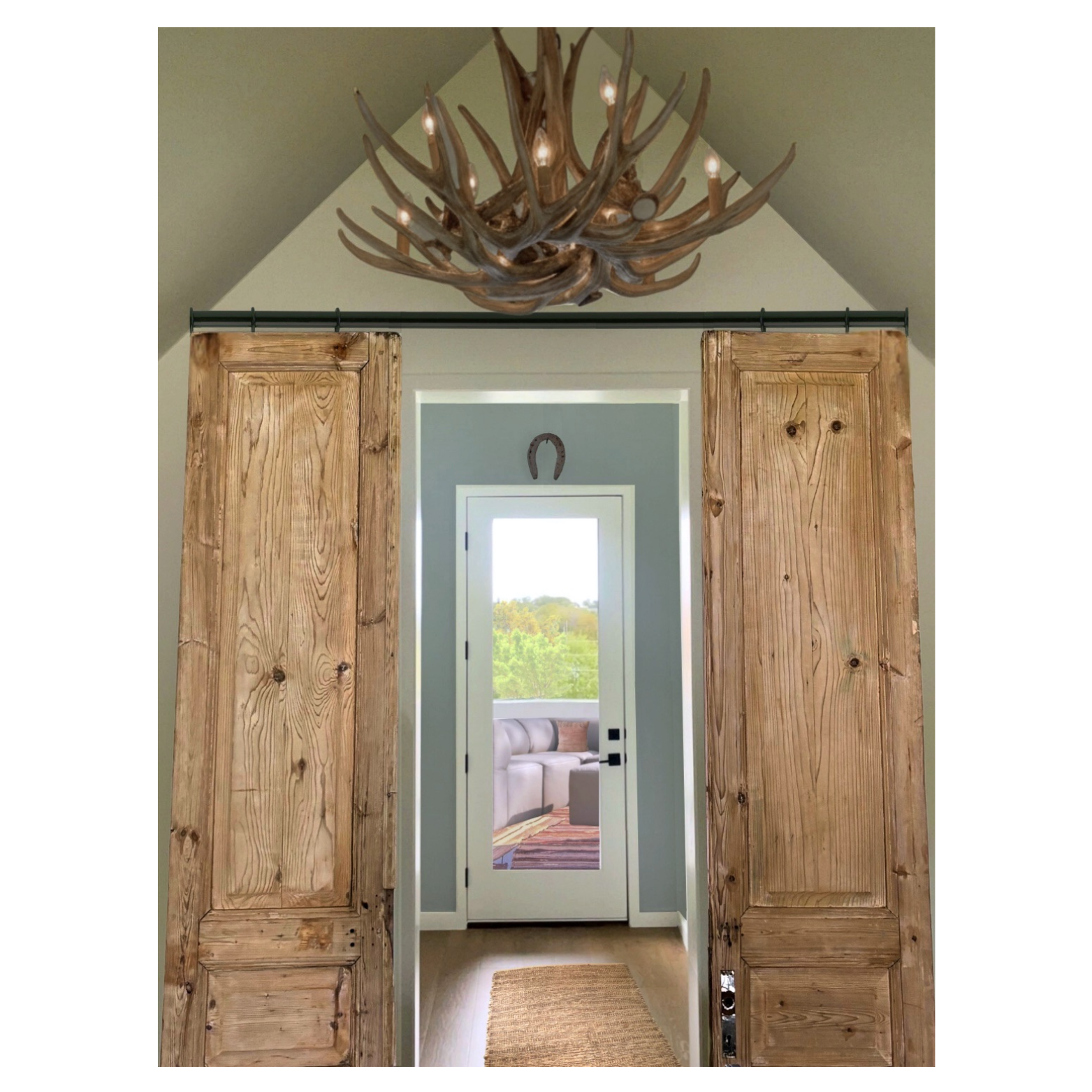 A room designed by Austin interior designer HOLLEYHOUSE with a doorway with sliding wooden barn doors, an antler chandelier hanging from the ceiling, and a view into a bright room with a window and sofa outside.