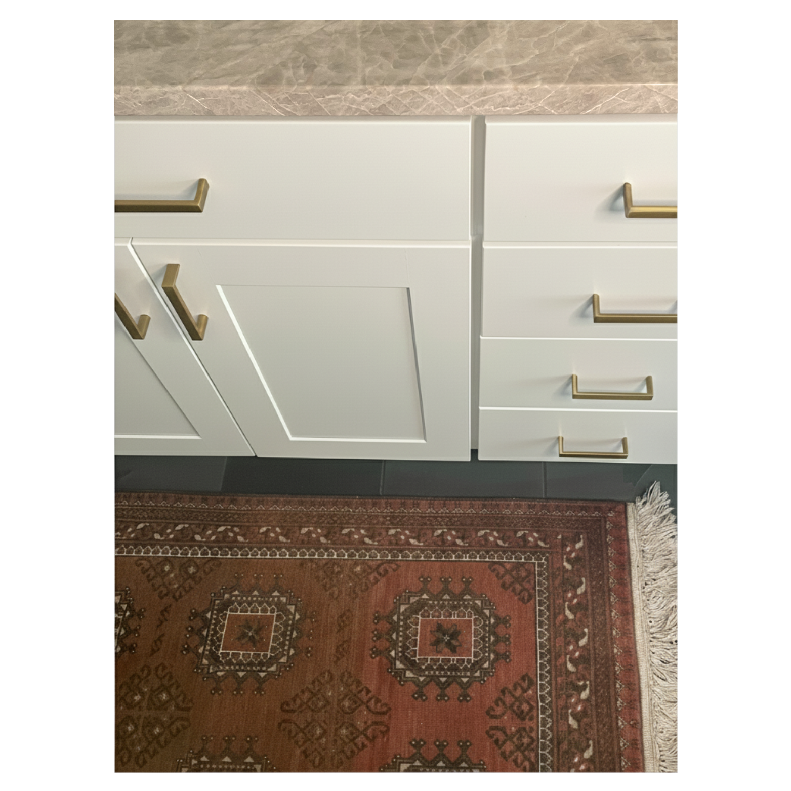 Close-up of kitchen designed by Austin interior designer HOLLEYHOUSE with white cabinets and gold handles, a marble countertop, and a red patterned rug on the floor.