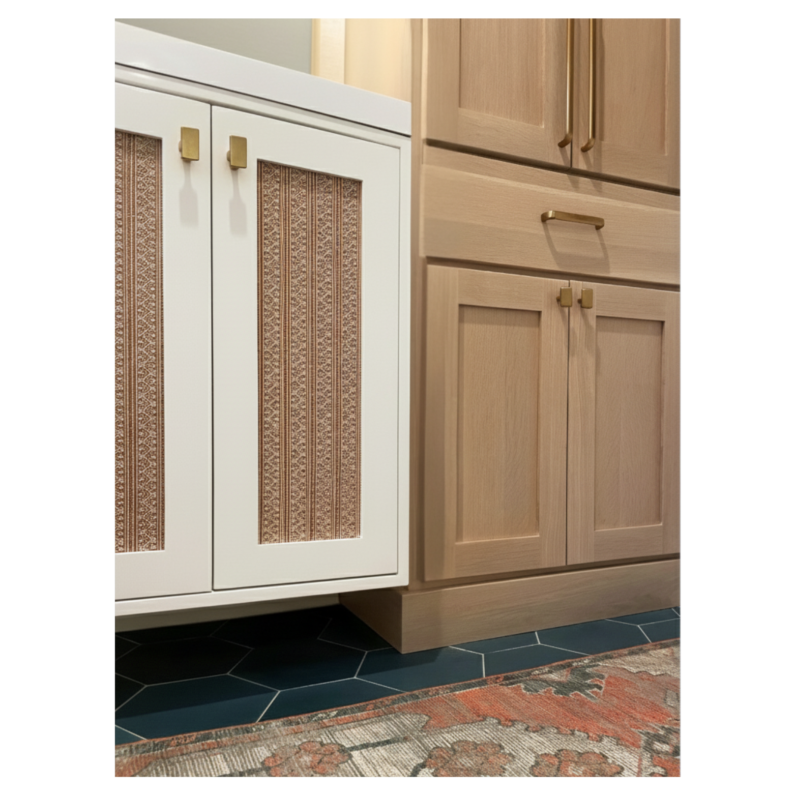 Kitchen designed by Austin interior designer HOLLEYHOUSE with two types of cabinets: one with white frame and patterned wood inserts, and the other with natural wood finish. Part of a decorative rug and black hexagonal floor tiles at the bottom.