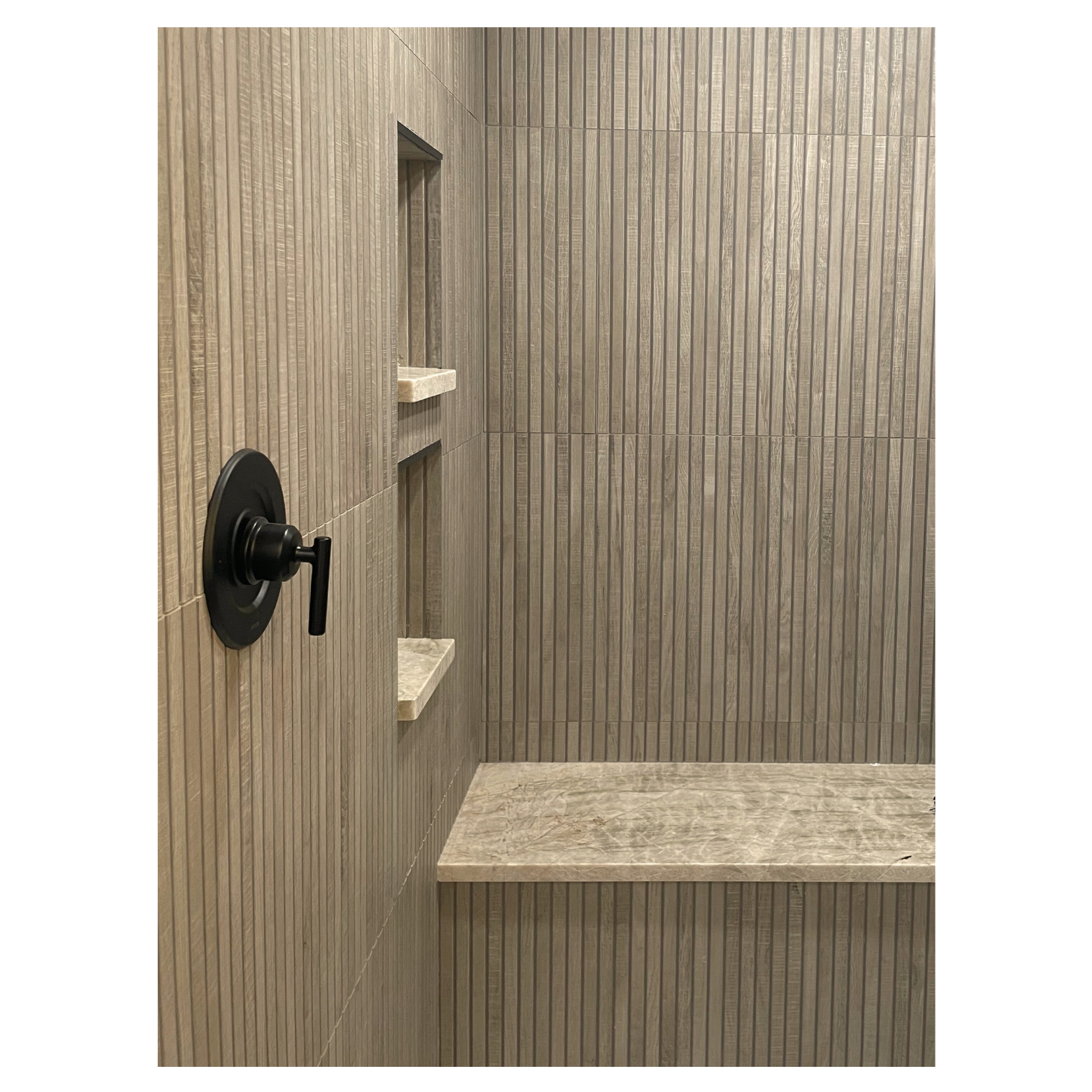 Bathroom shower designed by Austin interior designer HOLLEYHOUSE with beige tiled walls, built-in shelves, and a black shower handle.