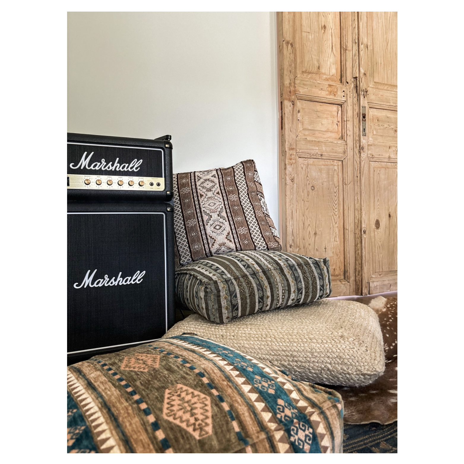 Room designed by Austin interior designer HOLLEYHOUSE with vintage-patterned couch with a rolled cushion and decorative pillow, a black Marshall guitar amplifier, and wooden double doors in the background.