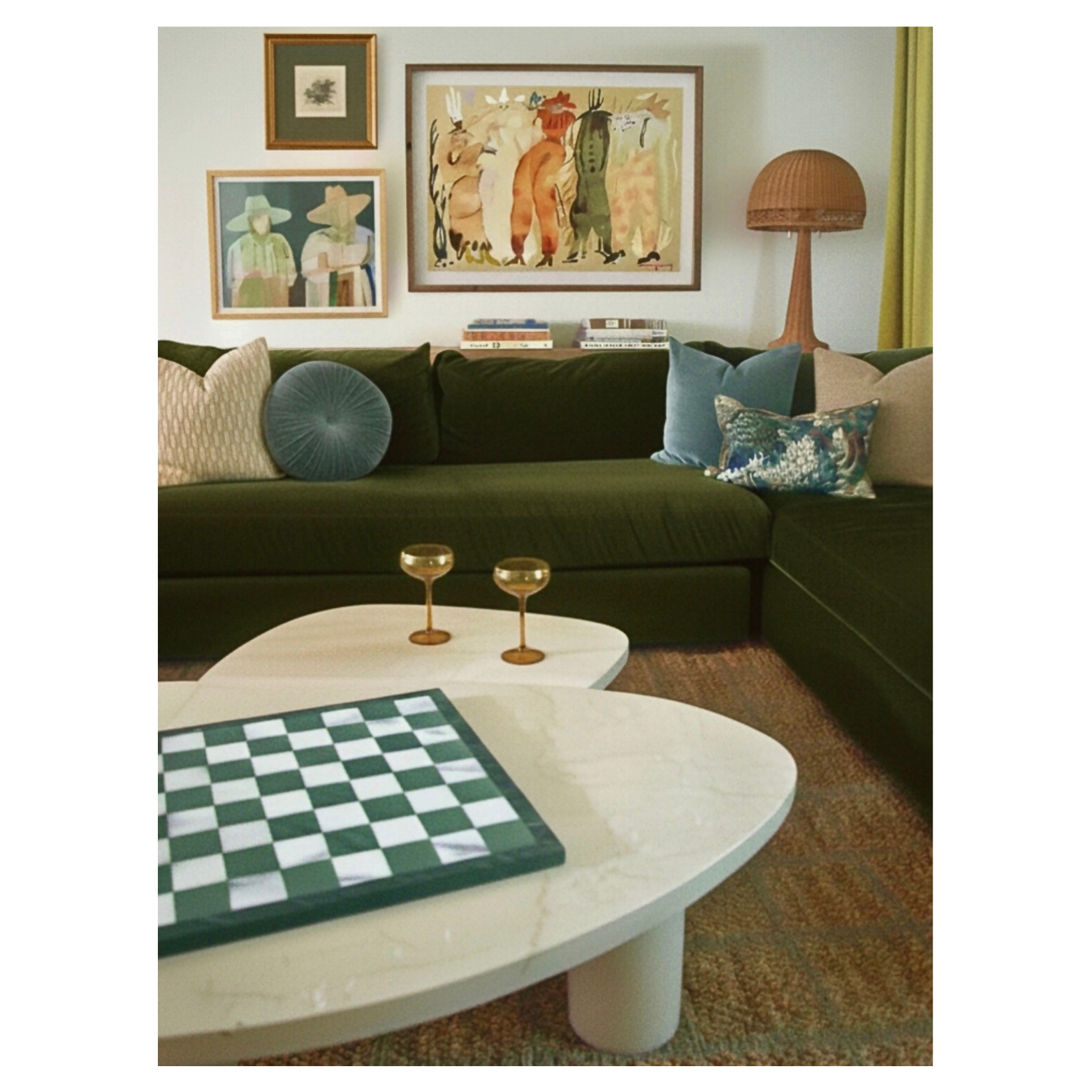 Living room designed by Austin interior designer HOLLEYHOUSE with a dark green sectional sofa, decorative pillows, wall art, a wooden floor lamp, a coffee table with a chessboard, and two gold-rimmed glasses.