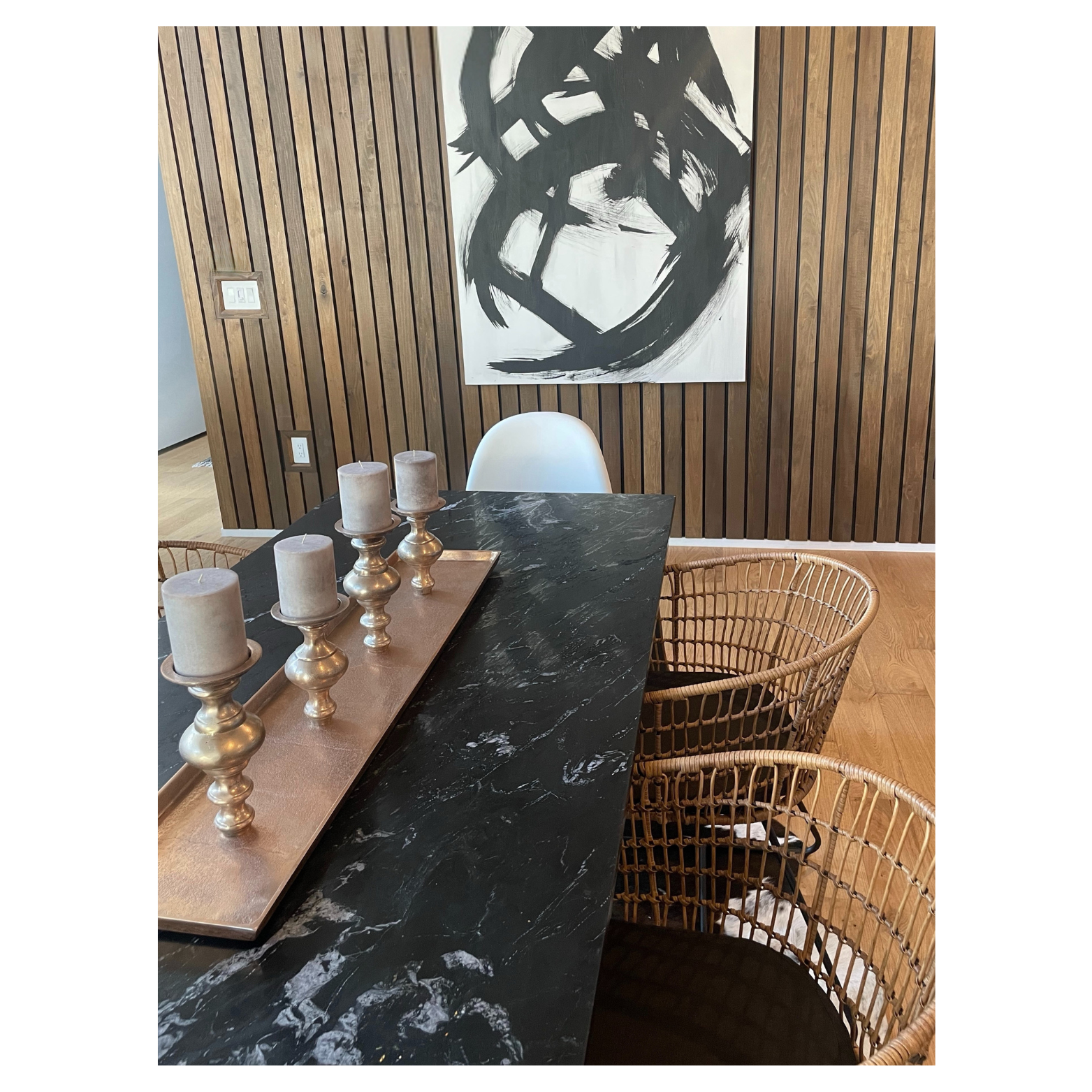 Dining room designed by Austin interior designer HOLLEYHOUSE with a black marble table, wicker chairs, a wooden accent wall, and abstract black and white artwork.