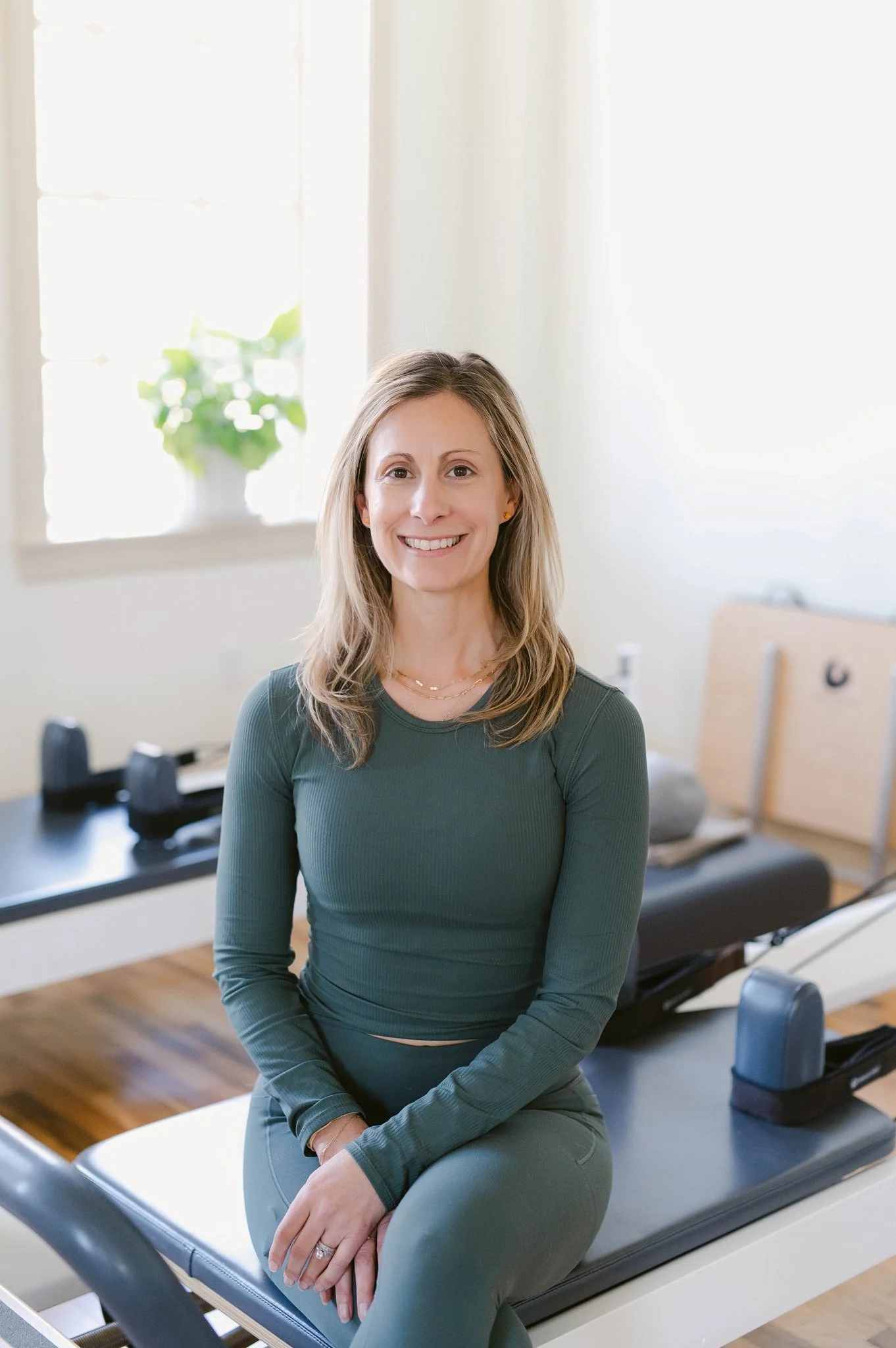 Pilates studio owner woman sitting on a reformer smiling, representing successful studio growth with Bloom Analytics