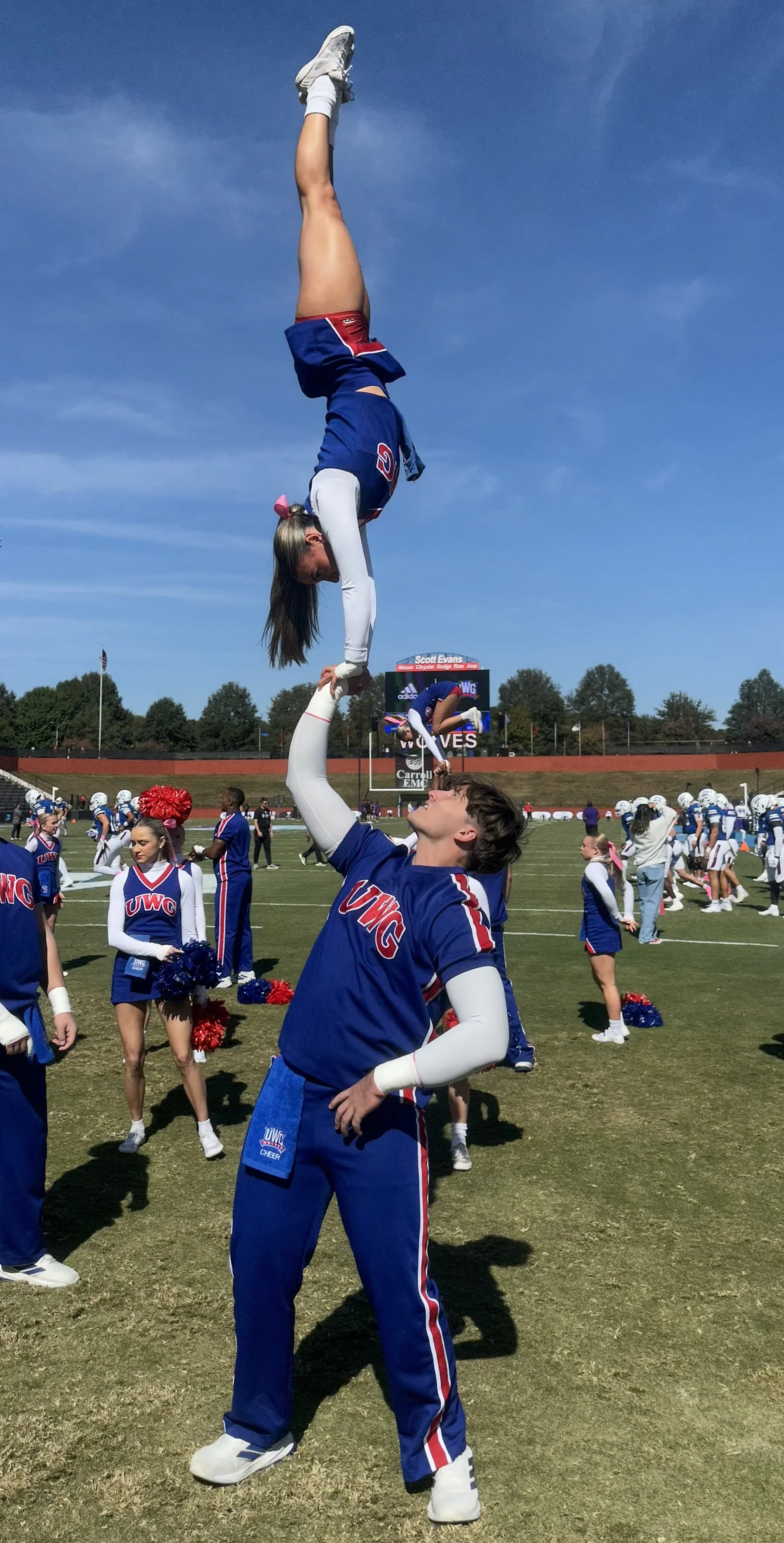 Coach Mike performing a coed stunt during a cheer competition on the field.