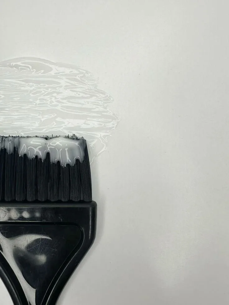 Close-up of a paintbrush with white paint on it, resting on a white surface.