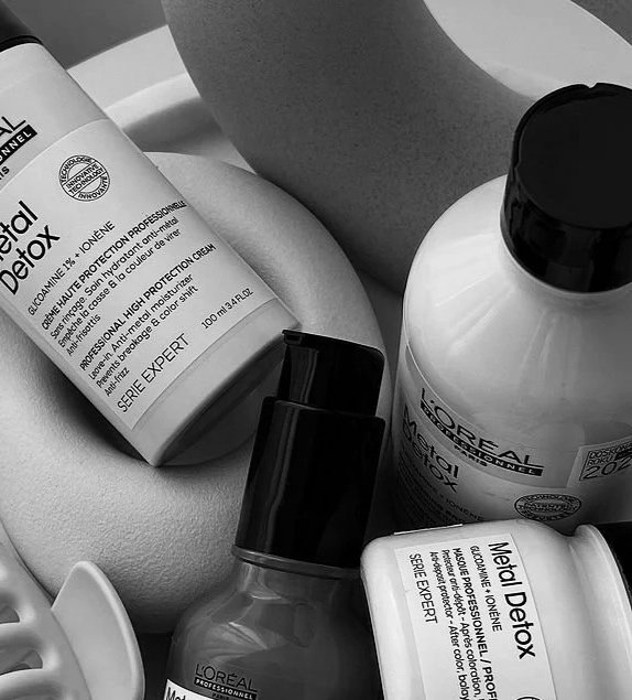 Black and white photo of haircare products, including bottles of L'OrΓ©al Metal Detox and a spray bottle, arranged on a light surface.