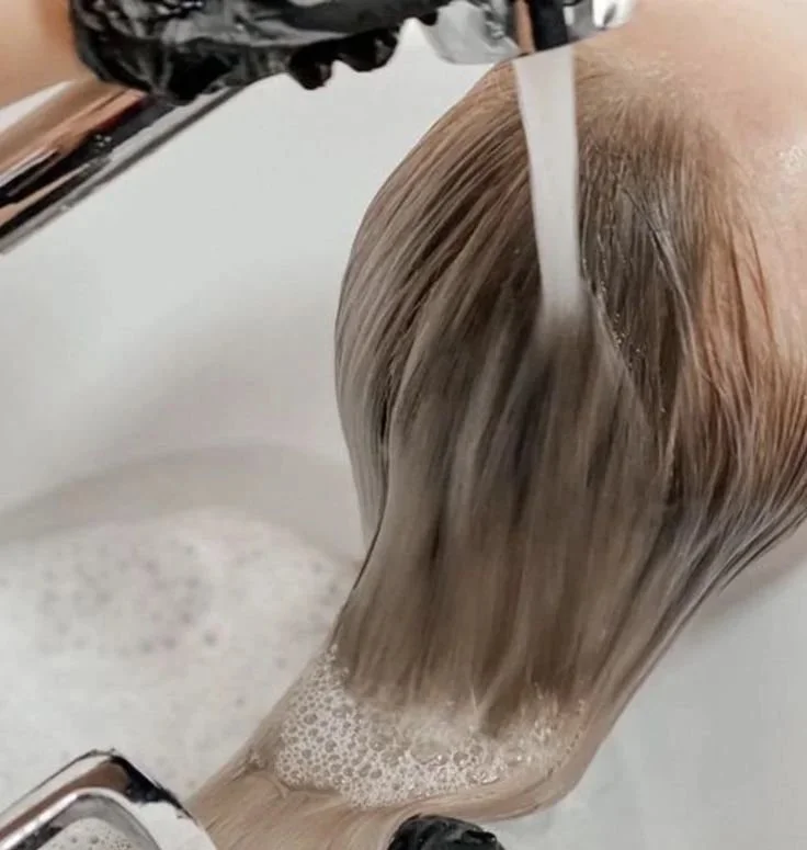 Person washing their blonde hair in a sink with water and shampoo.