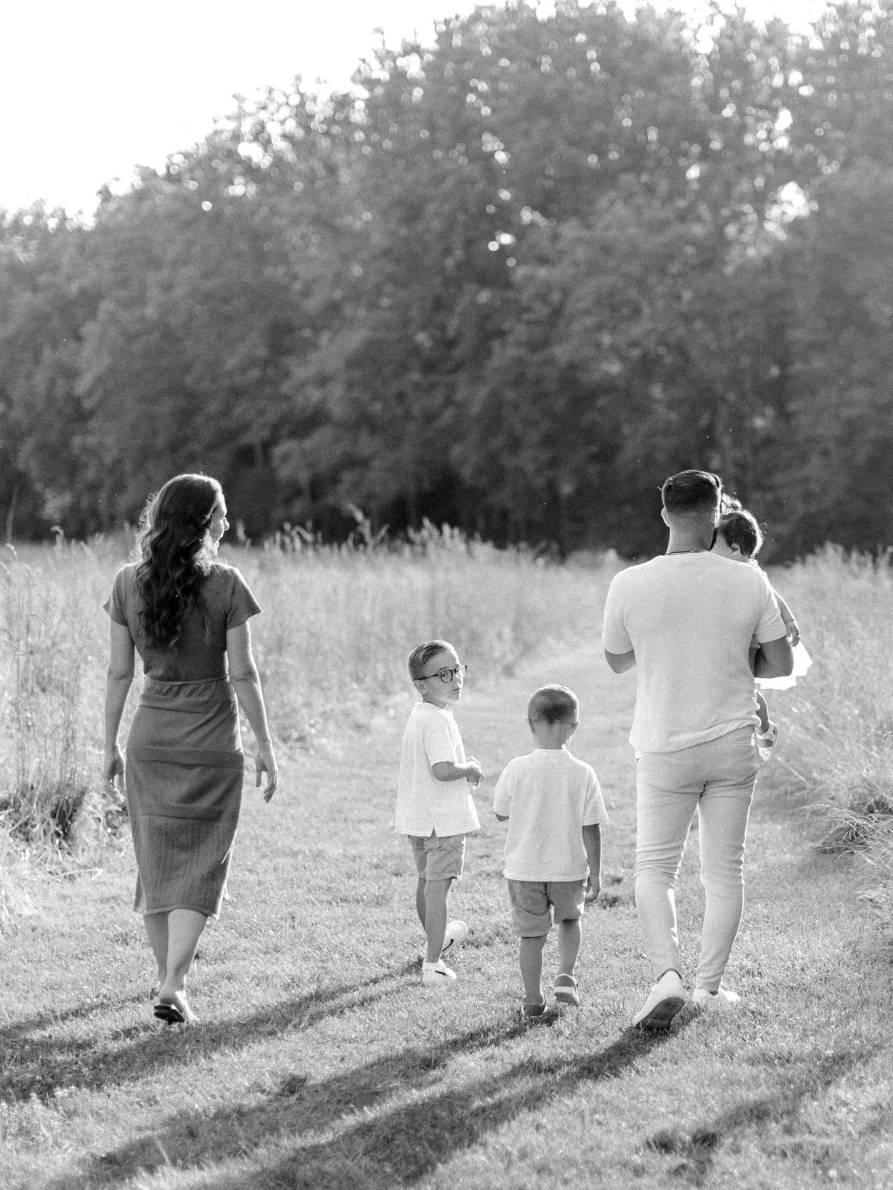 A family of six walking outdoors on a sunny day, with trees in the background. The scene is in black and white.