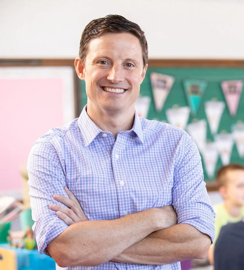 Scott Baldermann, a smiling man with crossed arms, in a classroom setting.