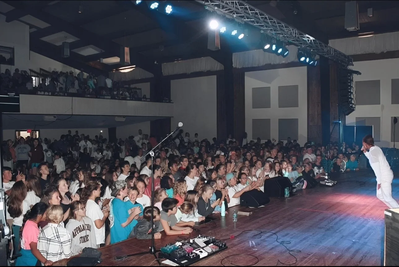 Large Christian hip-hop concert with an energized crowd cheering as a performer(Brea Miles) bows on stage under bright concert lighting.