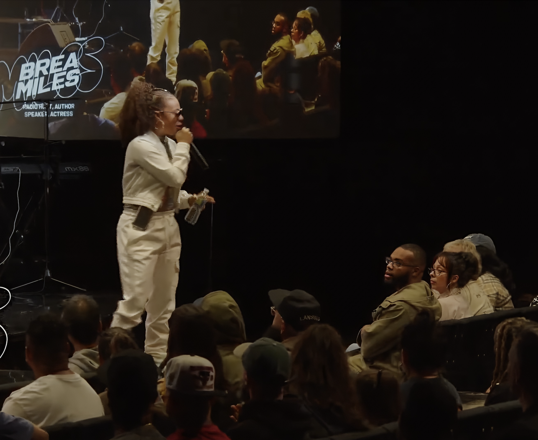 Keynote speaker Brea Miles presenting at a faith-based leadership and mentorship conference in Tampa, Florida. the speaker addresses an engaged audience while a large screen behind displays event topics and visuals.