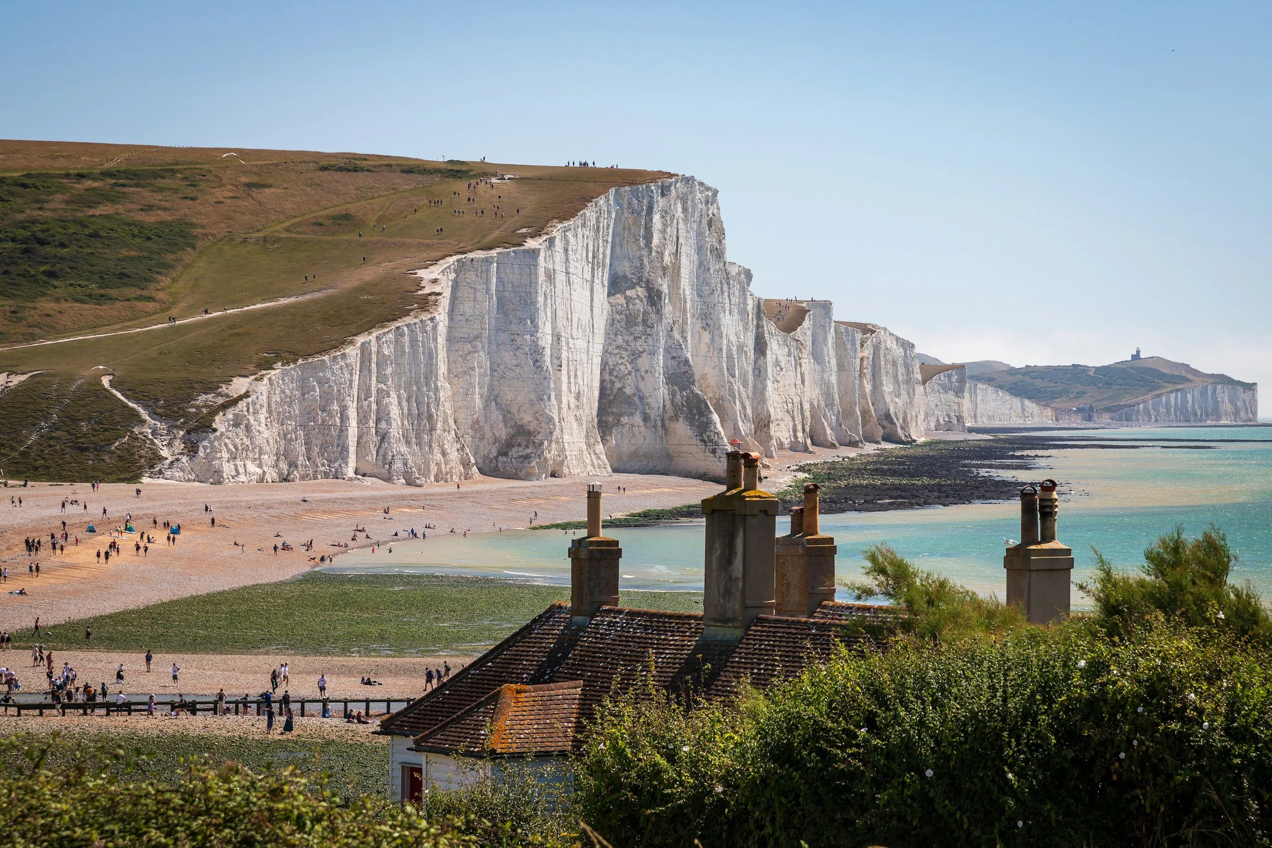 Cliffs of Dover with white chalk formations overlooking a pebble beach and the sea, with rooftops and chimneys in the foreground.