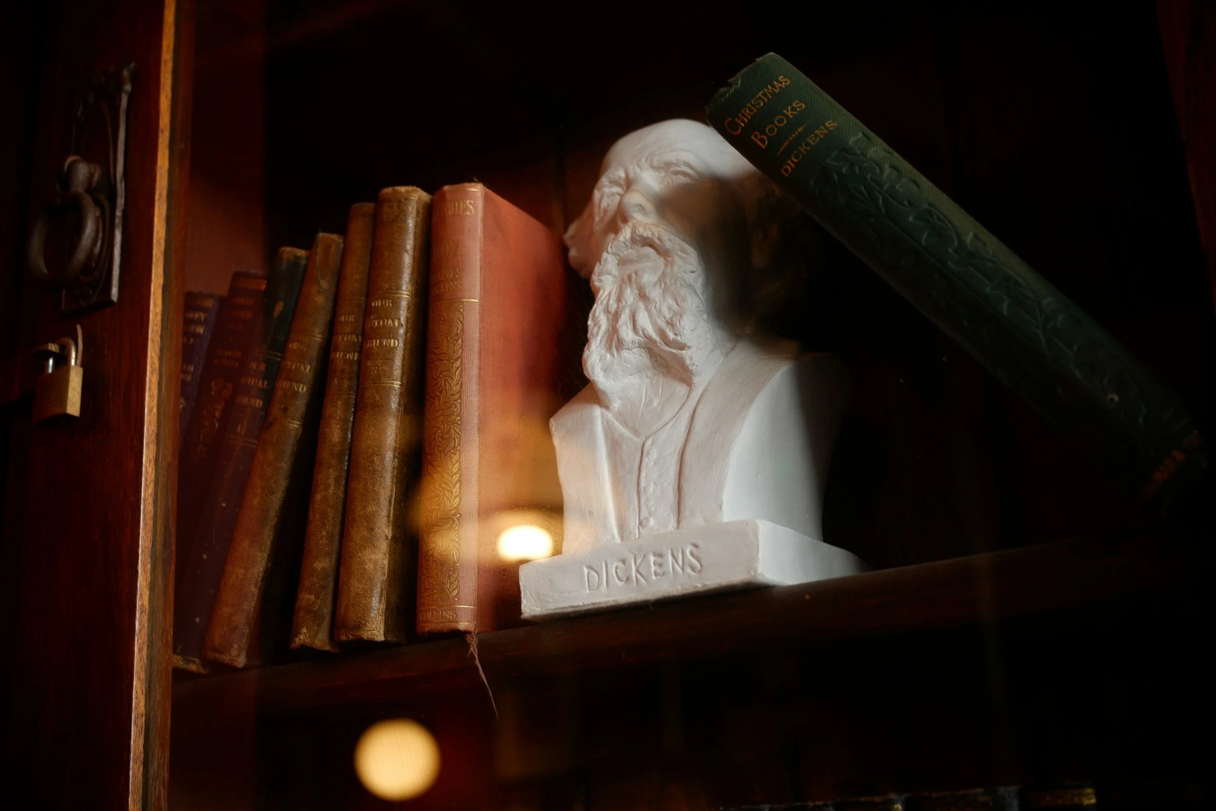 A bookshelf with a white bust of a man labeled 'Dickens' and a row of vintage books, one of which is titled 'Christmas Books'.
