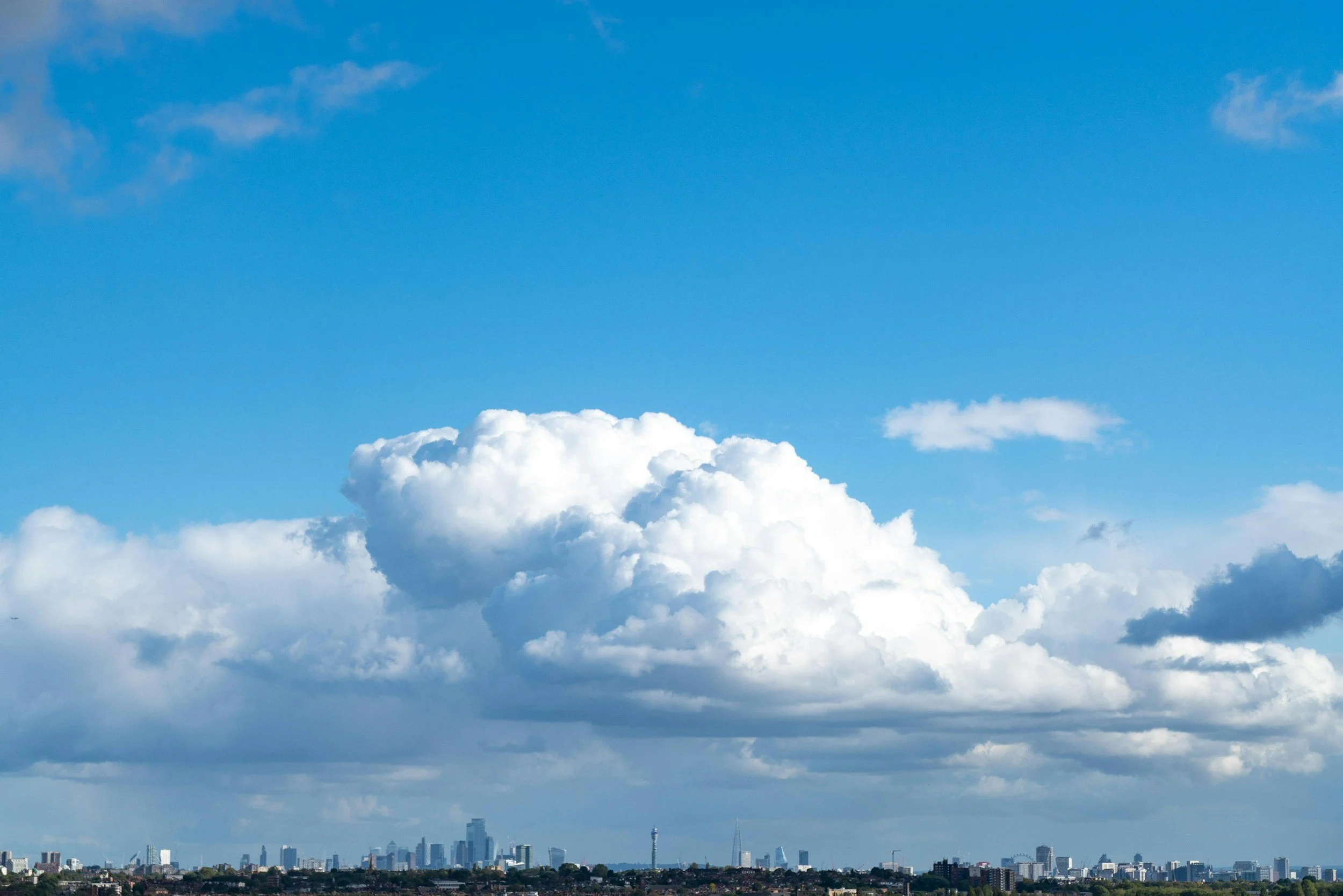 Sky filled with large white cumulus clouds over a cityscape with tall buildings and skyscrapers.