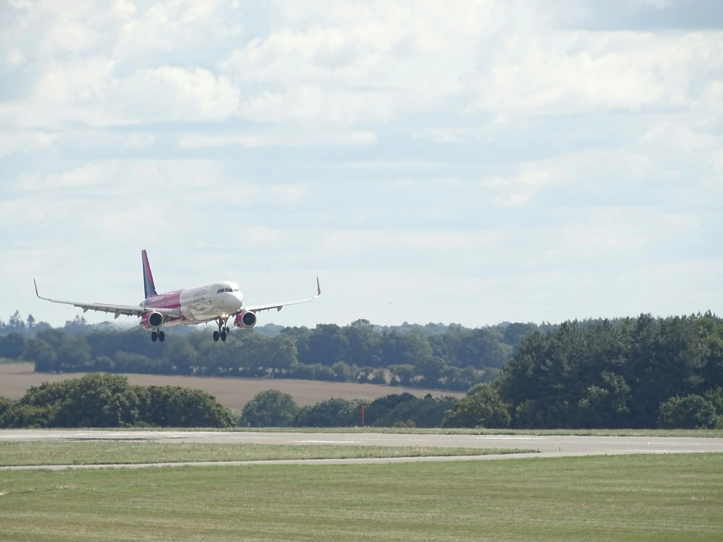 An airplane landing on a runway surrounded by grassy fields and trees, under a partly cloudy sky.