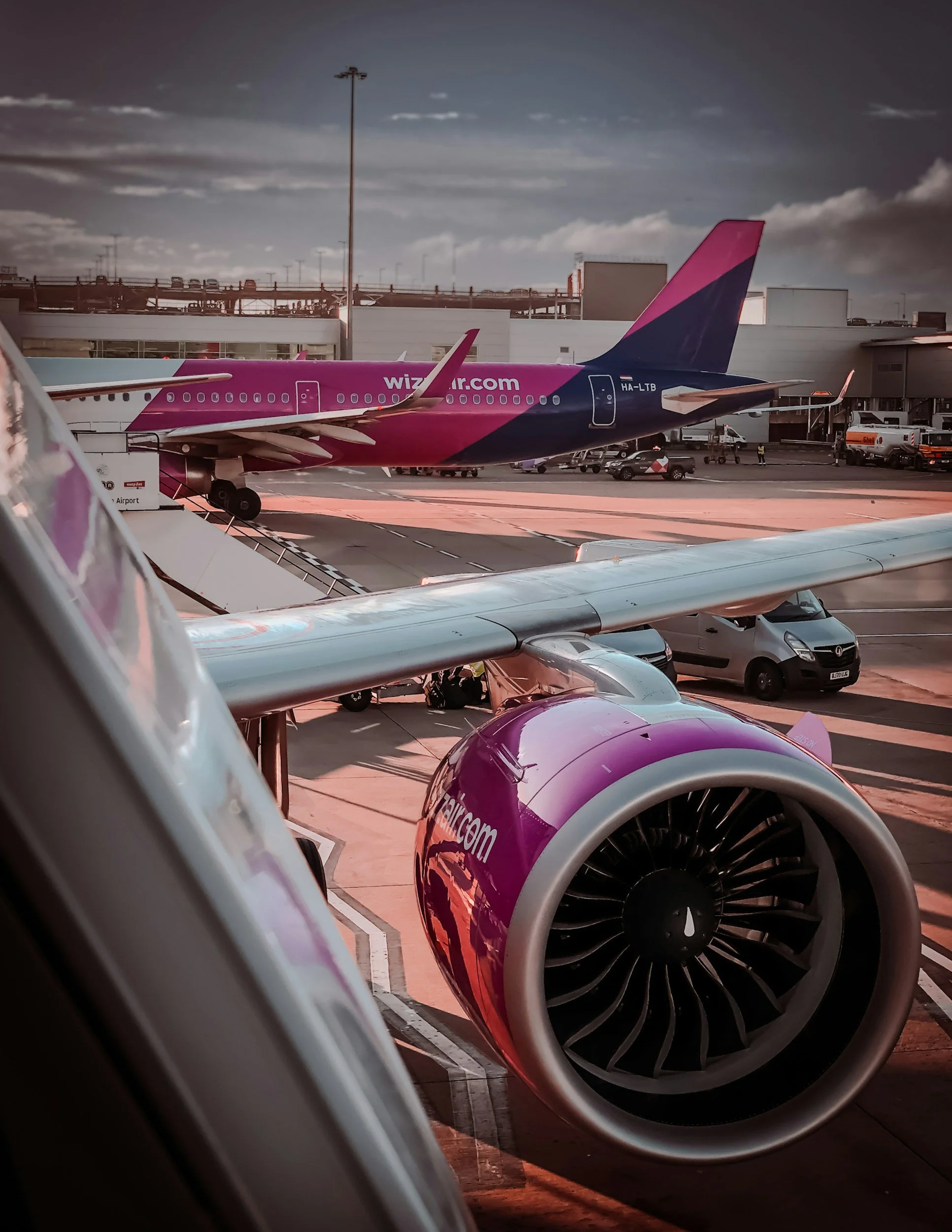 View of an airplane engines with pink and purple livery on the tarmac at an airport, with other airport vehicles and buildings in the background.
