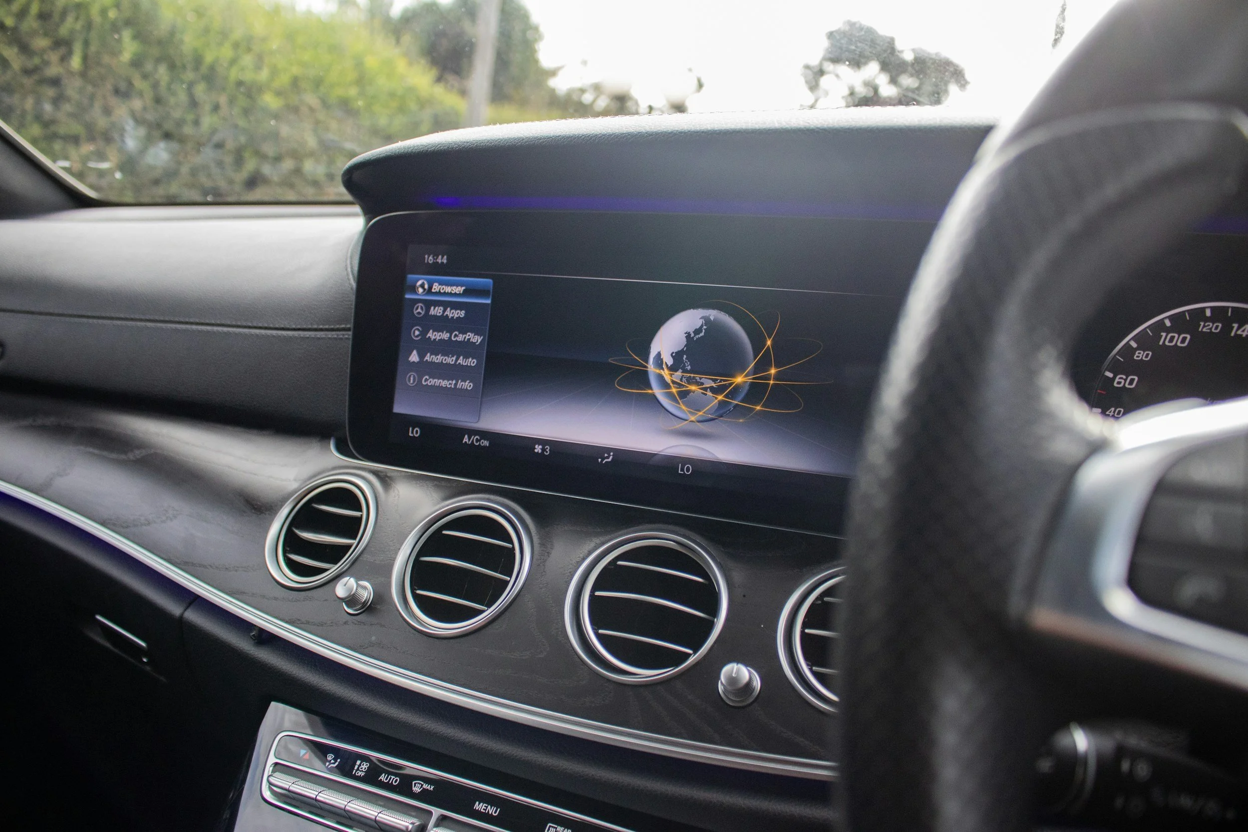 Interior of a car showing a digital dashboard and infotainment screen with options like Browser, MB Apps, Apple CarPlay, and Android Auto, with trees visible through the windshield.