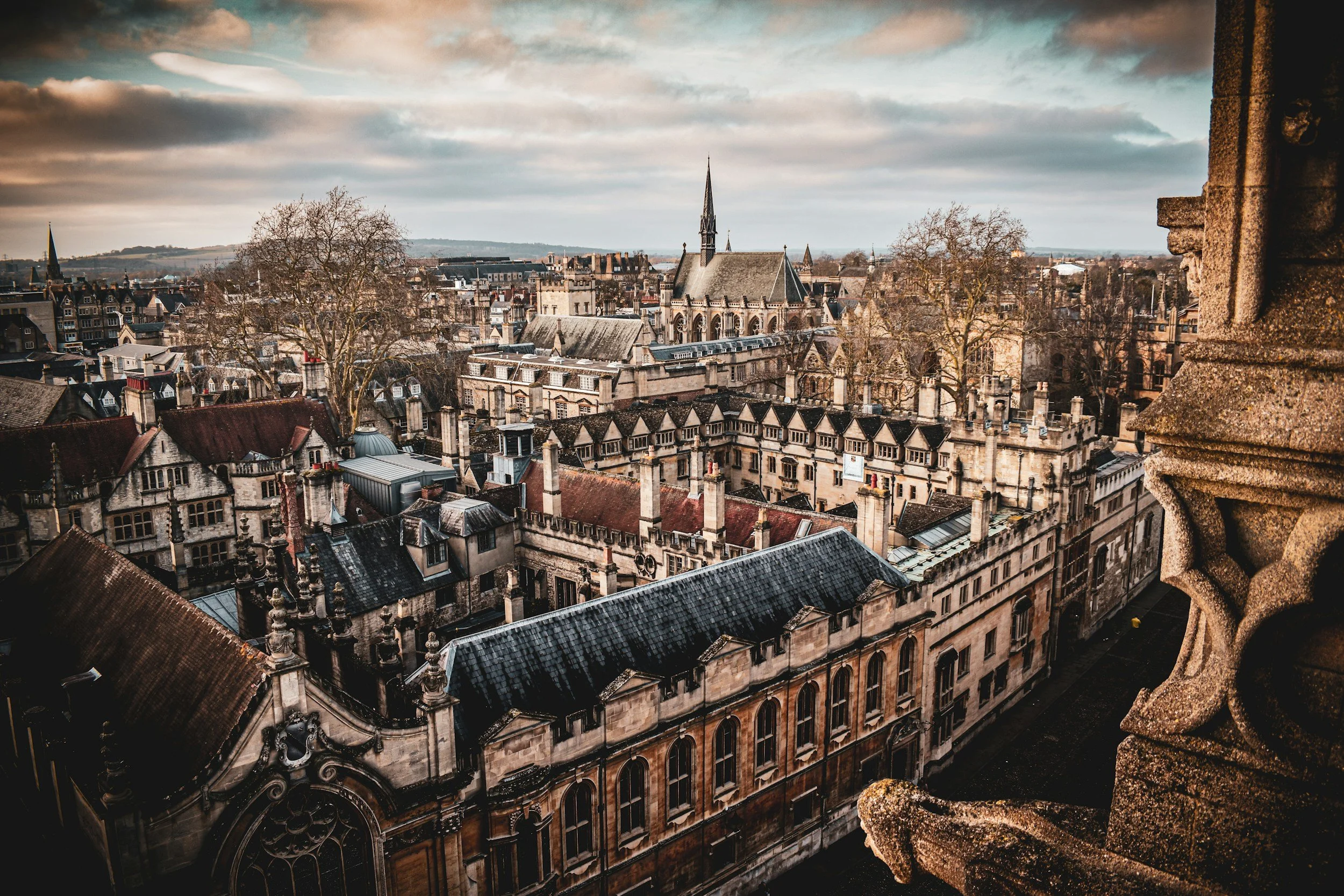 View of a historic European cityscape with a Gothic-style church and old buildings, seen from a high vantage point on a cloudy day.