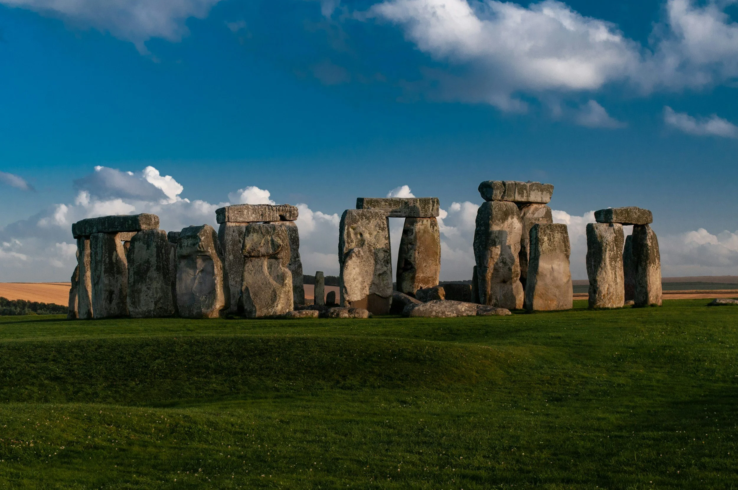 Stonehenge with large stone structures arranged in a circular formation on a grassy field under a partly cloudy sky.