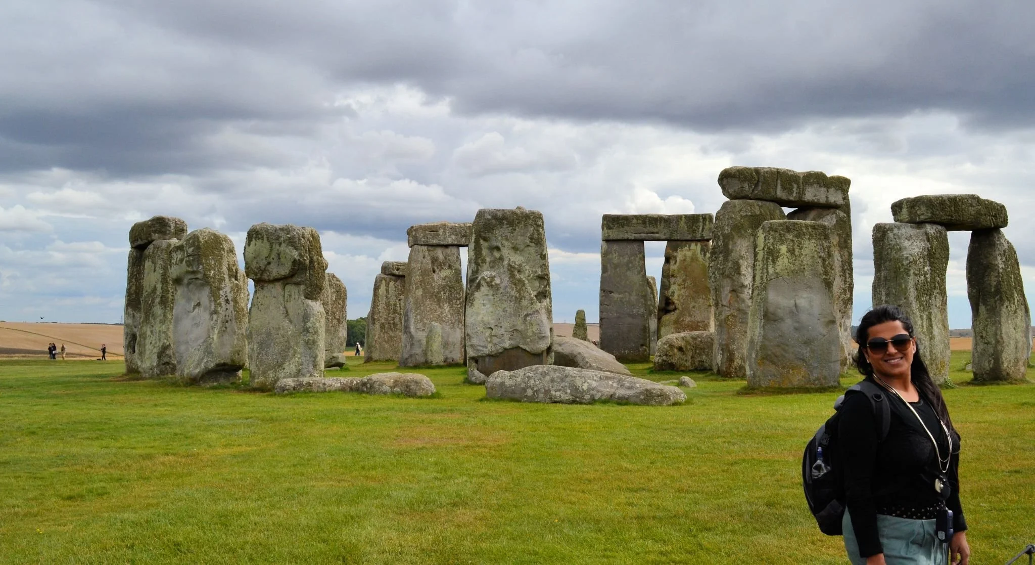 Tourists visiting Stonehenge on a cloudy day, with a woman smiling in the foreground.