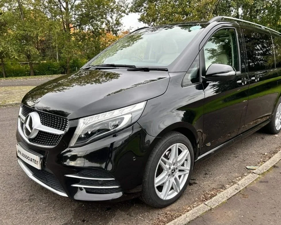 Black Mercedes-Benz van parked on a street with trees in the background.
