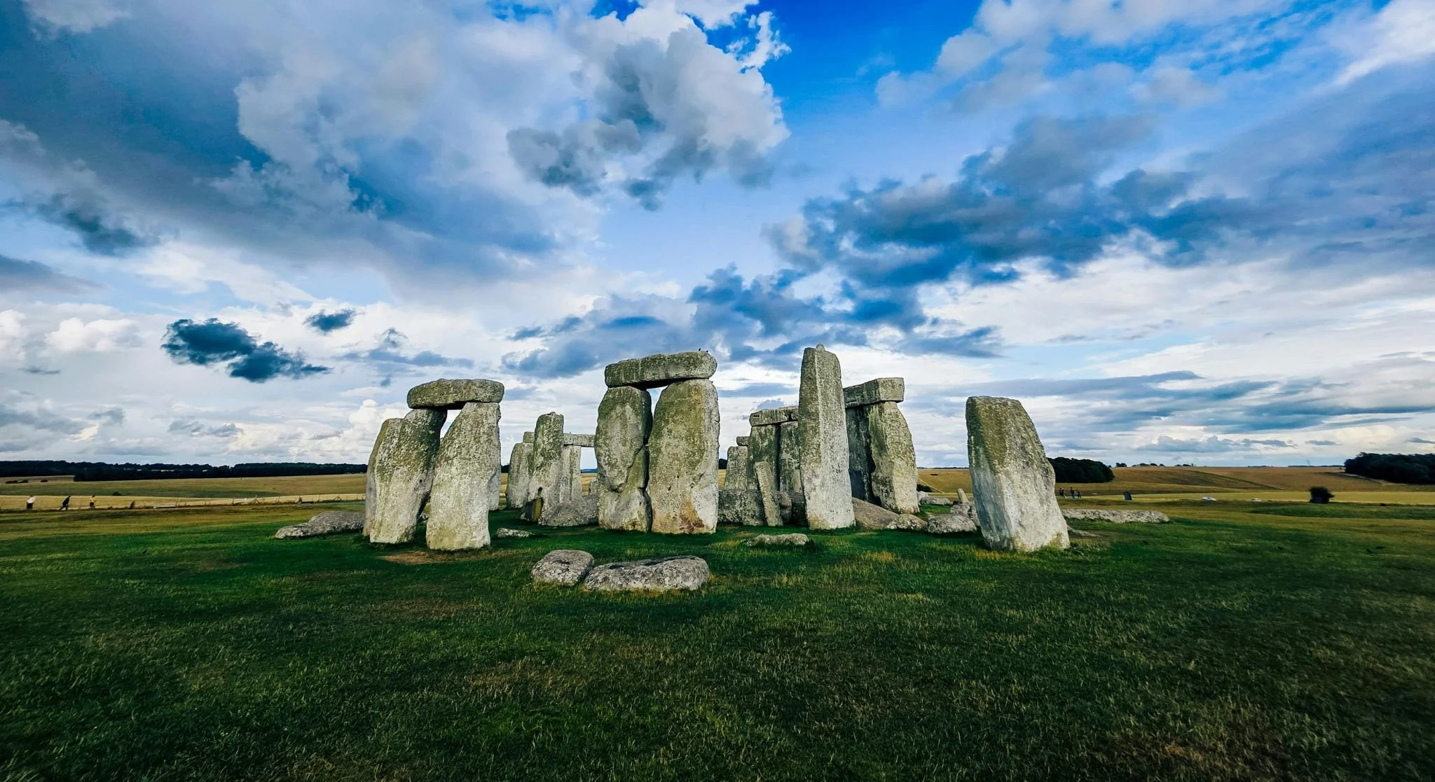 Stonehenge, a prehistoric monument with large upright stones arranged in a circular formation, set against a blue sky with scattered clouds and a green grassy field.