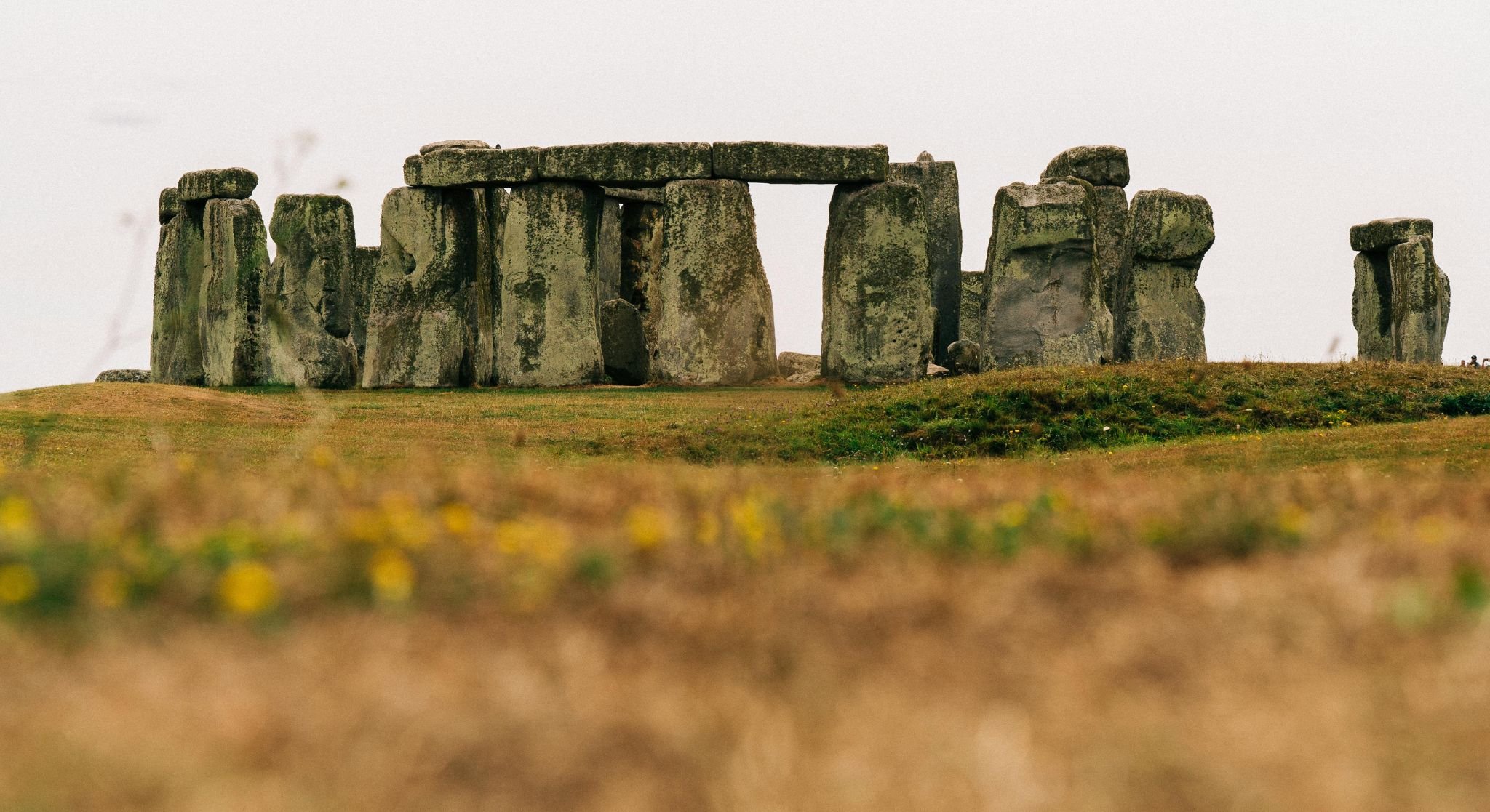 The image shows the historic site of Stonehenge with large standing stones arranged in a circular formation on a grassy landscape under an overcast sky.