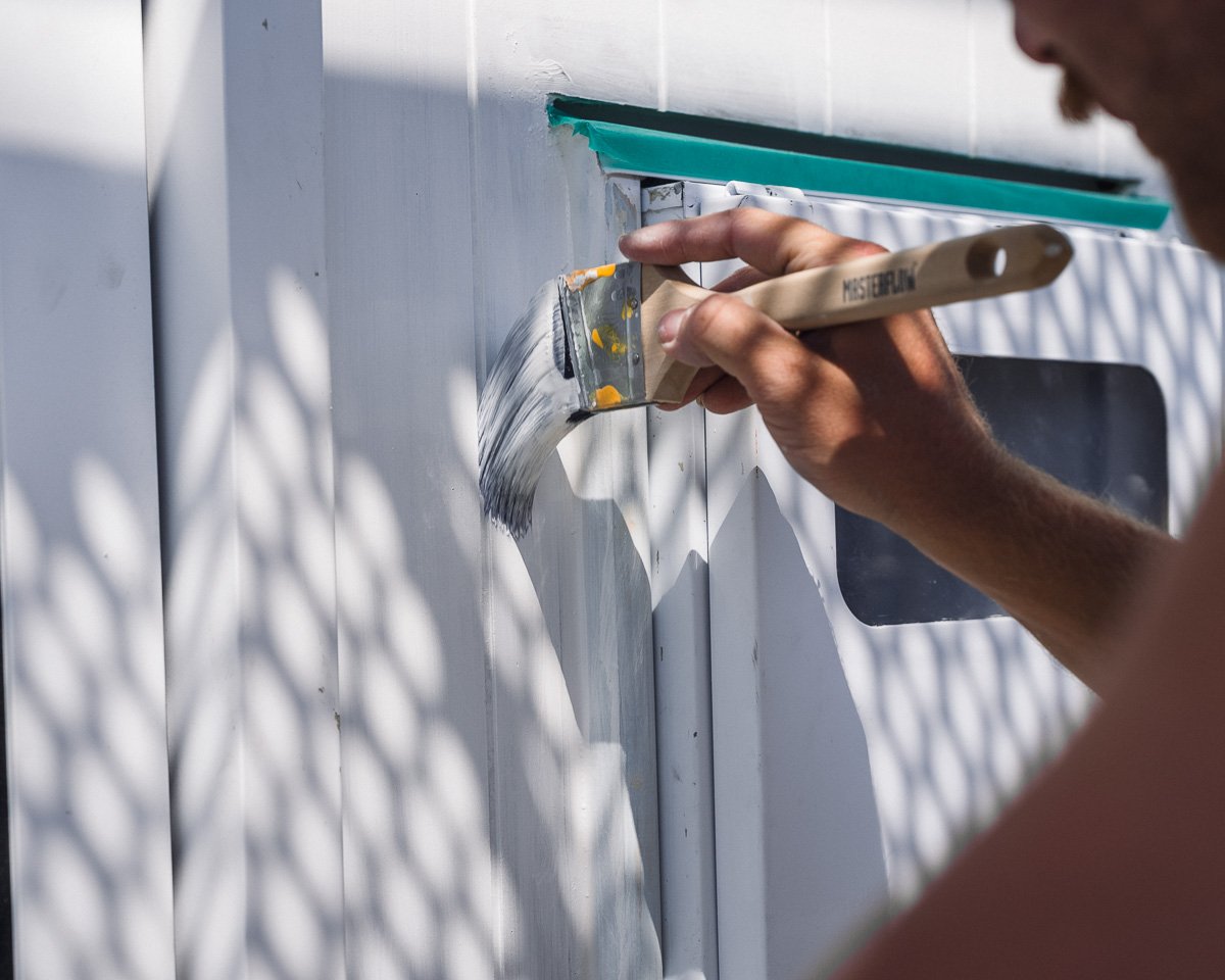 close up of person using paintbrush to paint exterior of new build house in a white colour