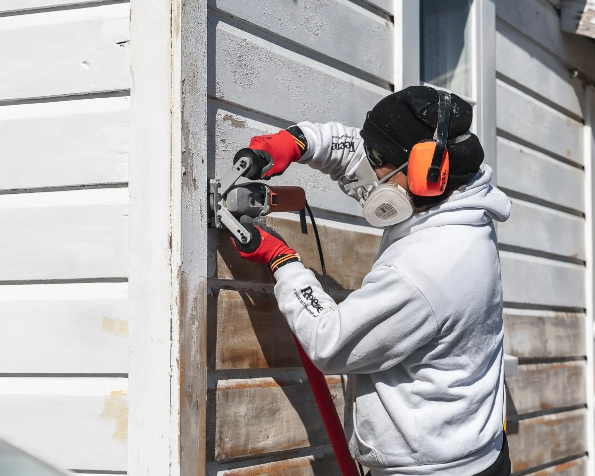 man wears white resene branded hoody holding paint shaver pro machine, he is stripping old cracked white paint off weatherboard exterior