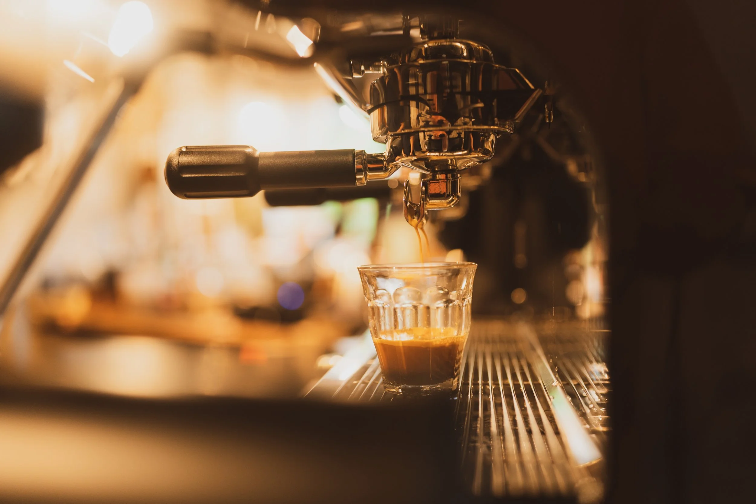 Close-up of a coffee machine dispensing espresso into a glass cup in a dimly lit cafe.