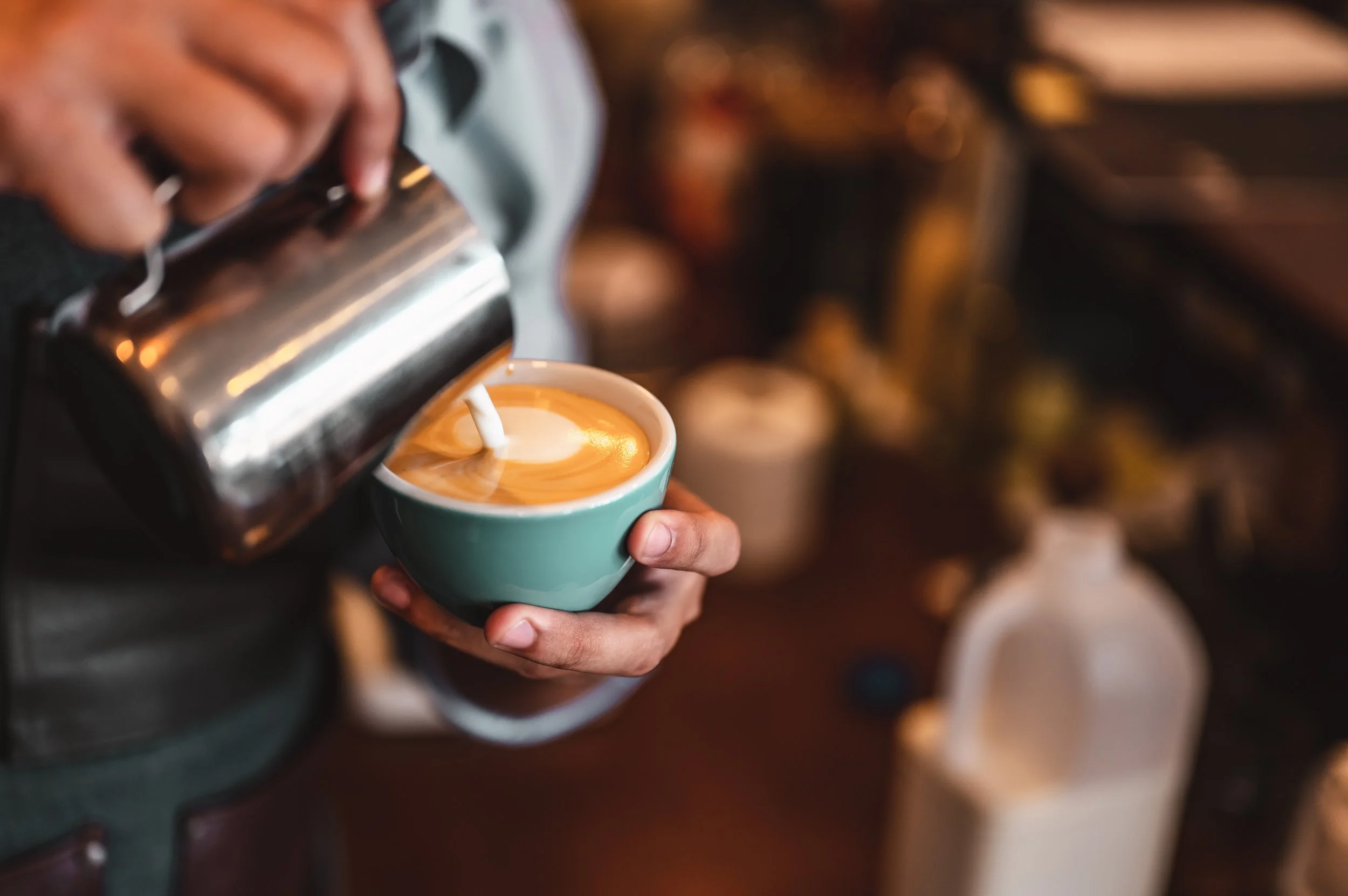 Barista pouring steamed milk into a cup of espresso to make a latte in a coffee shop.