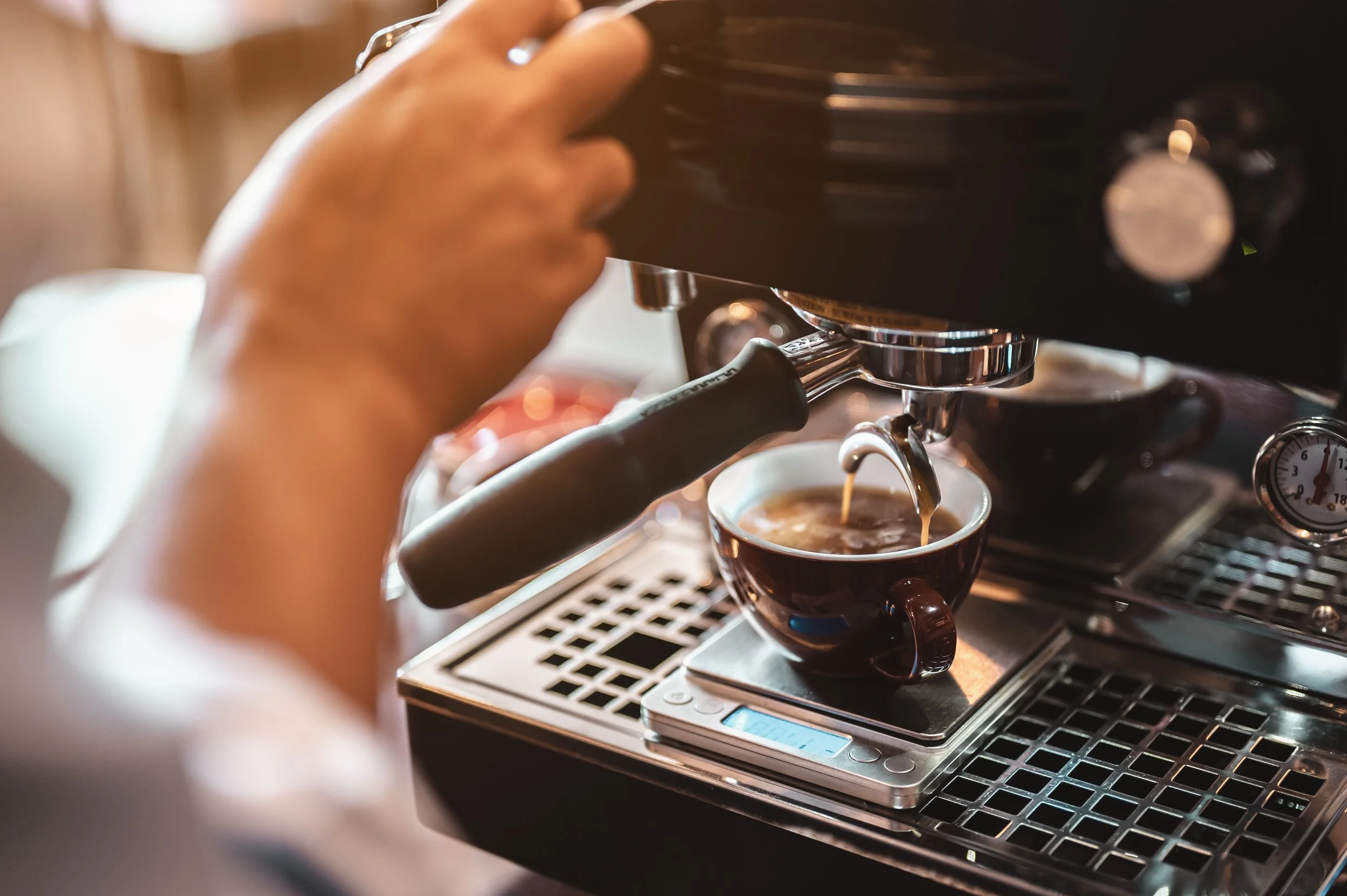 Close-up of a barista pulling espresso shots into two cups on a coffee machine, with one cup placed on a digital scale.