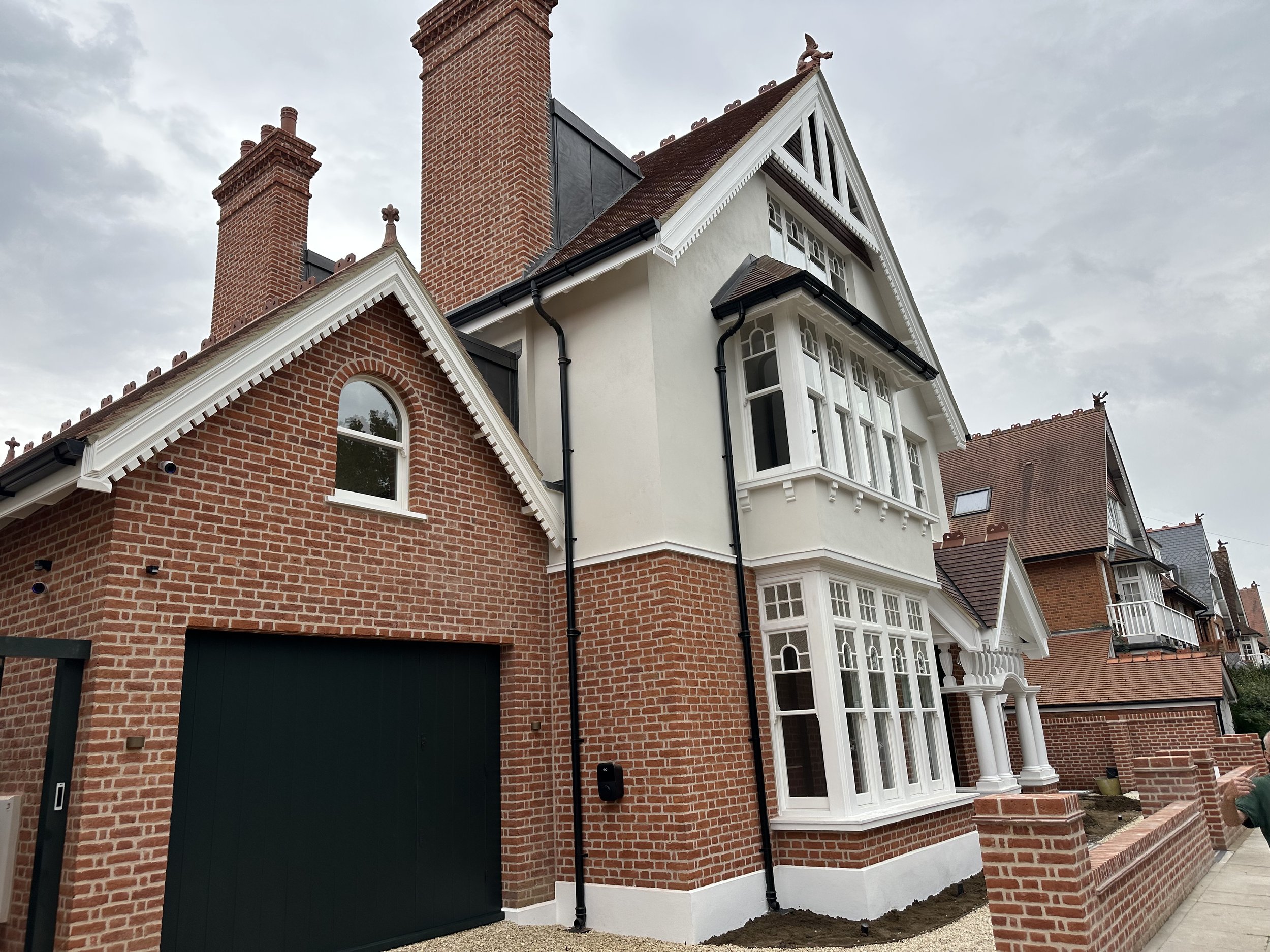 A large Victorian-style house with brick and white exterior, multiple gables, bay windows, and tall chimneys, under a cloudy sky.