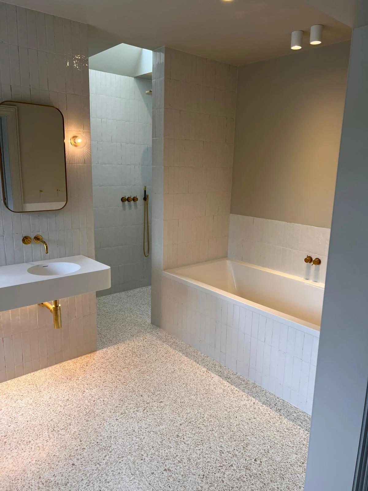 Modern bathroom with a white bathtub, a sink with brass fixtures, a mirror, a walk-in shower, and ceiling spotlights.