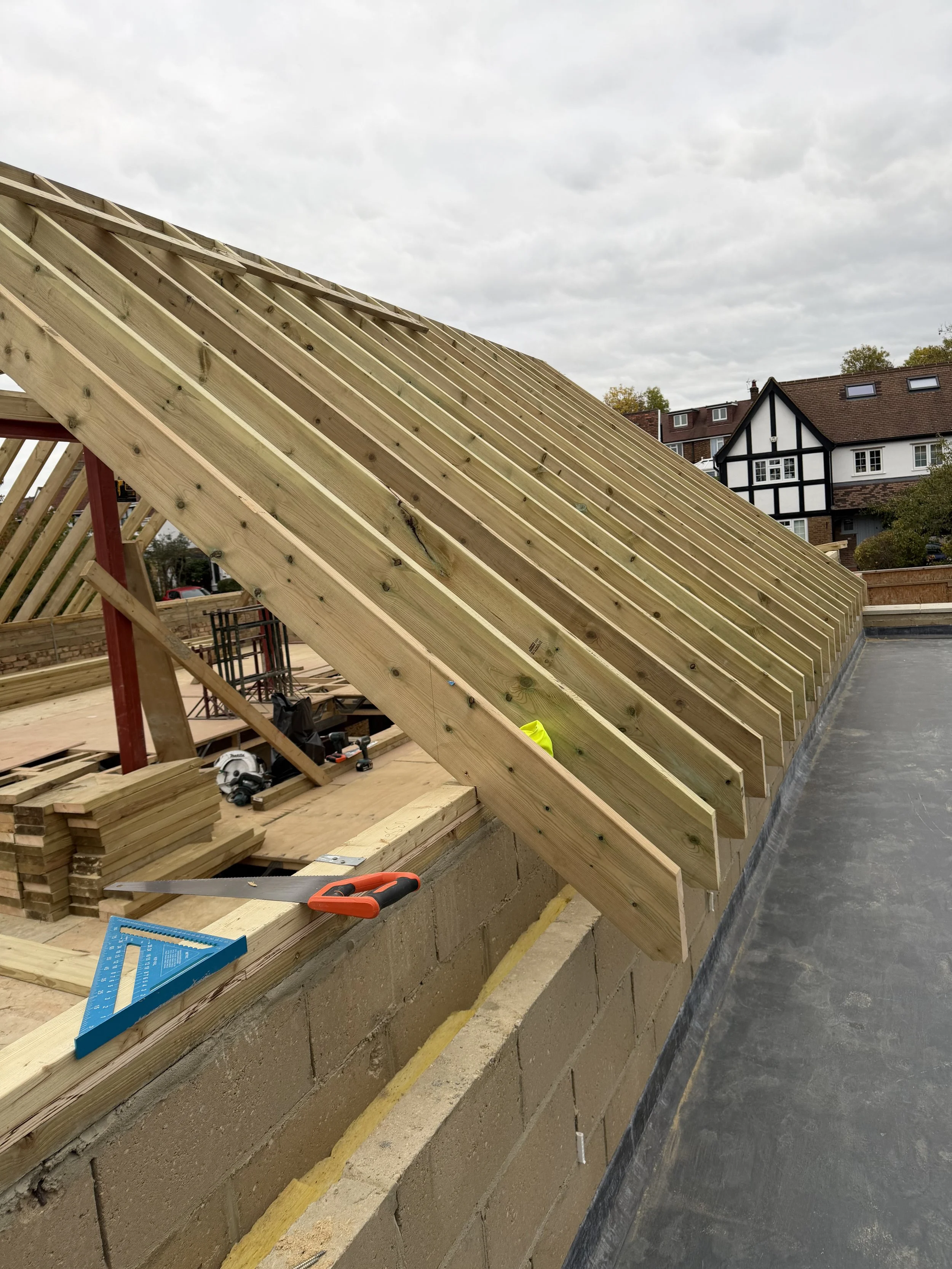 Construction site with wooden roof framing on a building under construction, tools and materials scattered around.
