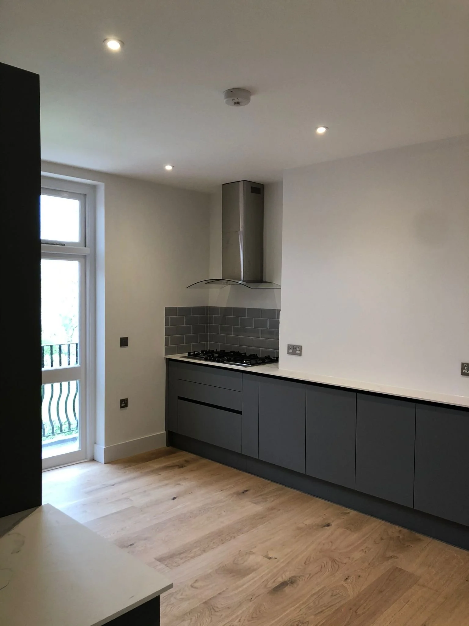 Modern kitchen with gray cabinets, gray tiled backsplash, wood flooring, white walls, and a window door leading outside
