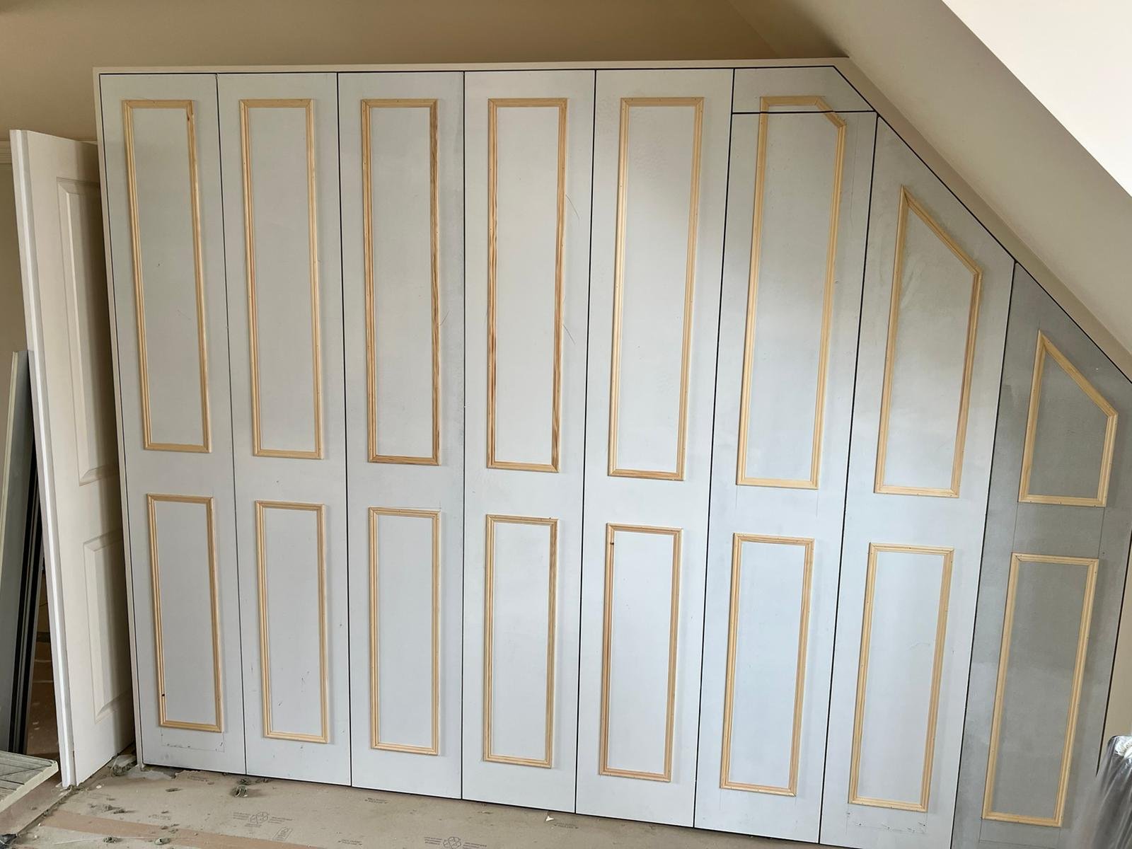 Panel closet doors with gold trim in a room with a sloped ceiling and a partially open door on the left.