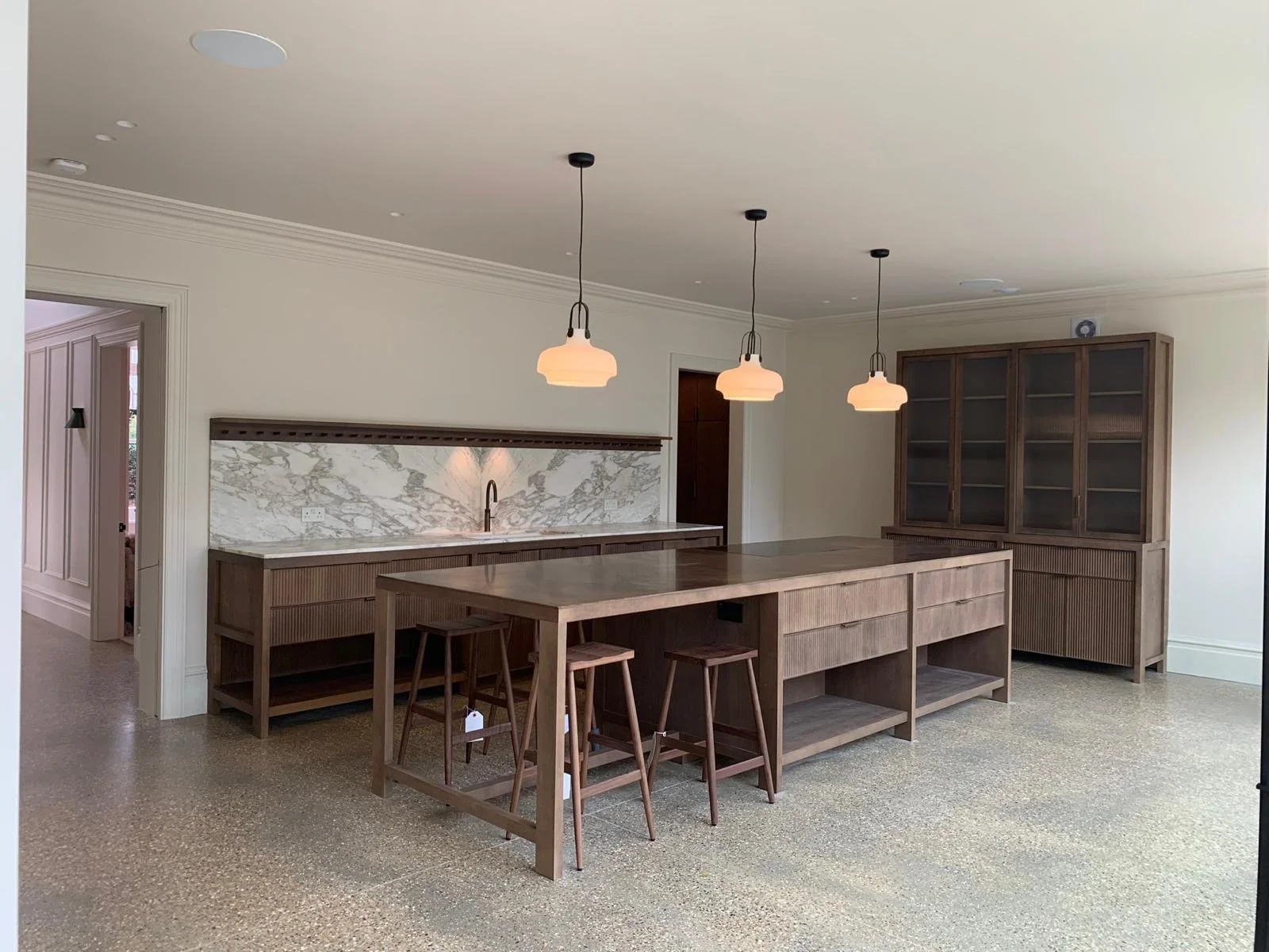 Modern kitchen with a large wooden island, pendant lighting, a marble backsplash, and a wooden cabinet with glass doors.