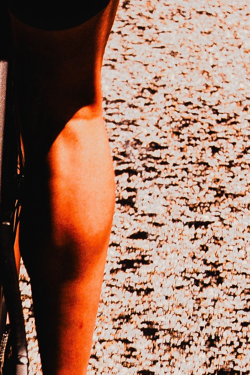 Une jambe d'une personne en short noir reposant sur un sol en gravier ou sable clair.