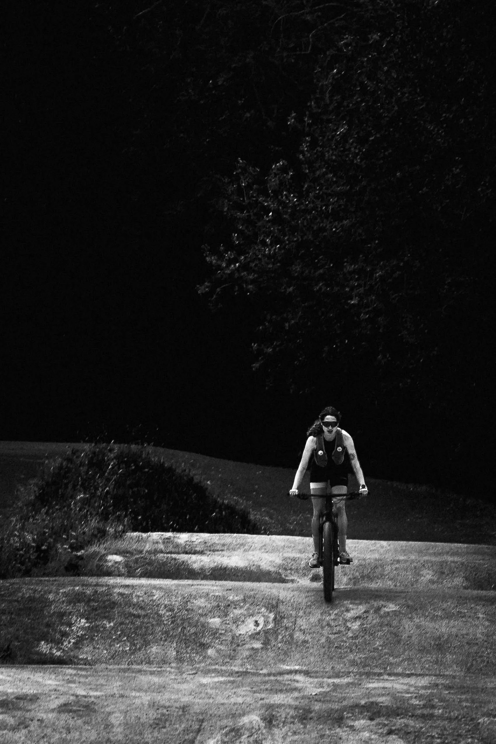 Une femme à vélo pédale sur un chemin de nuit, avec des arbres en arrière-plan.